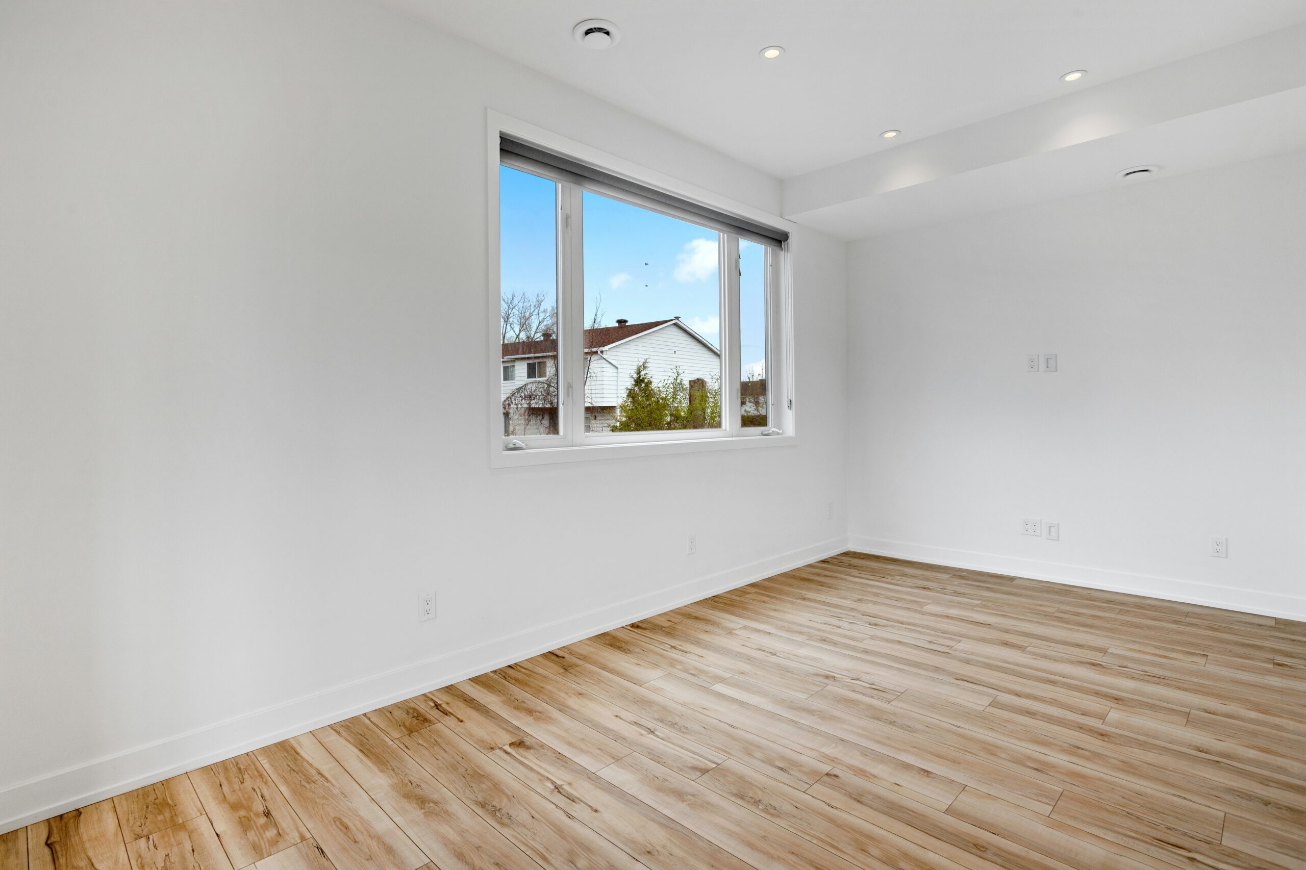 An empty room with wood floors and a window in a newly completed home