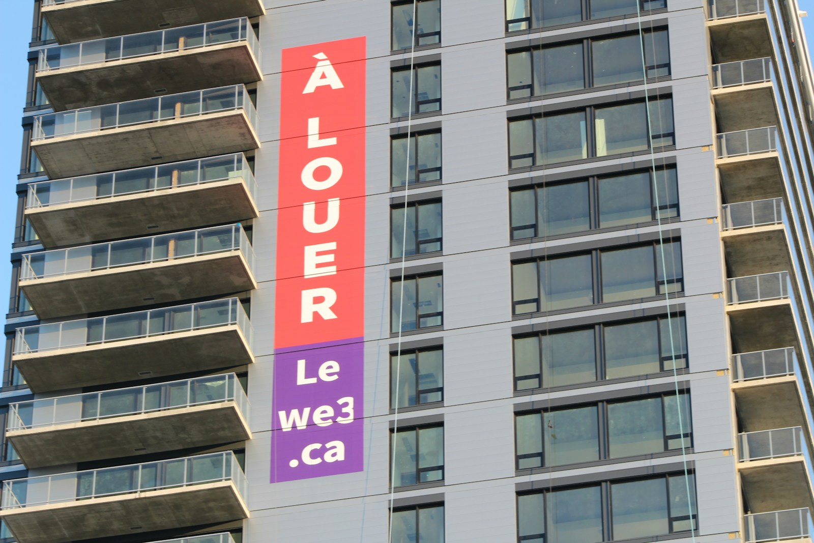 A large rental advertising banner hanging on the side of a modern apartment building