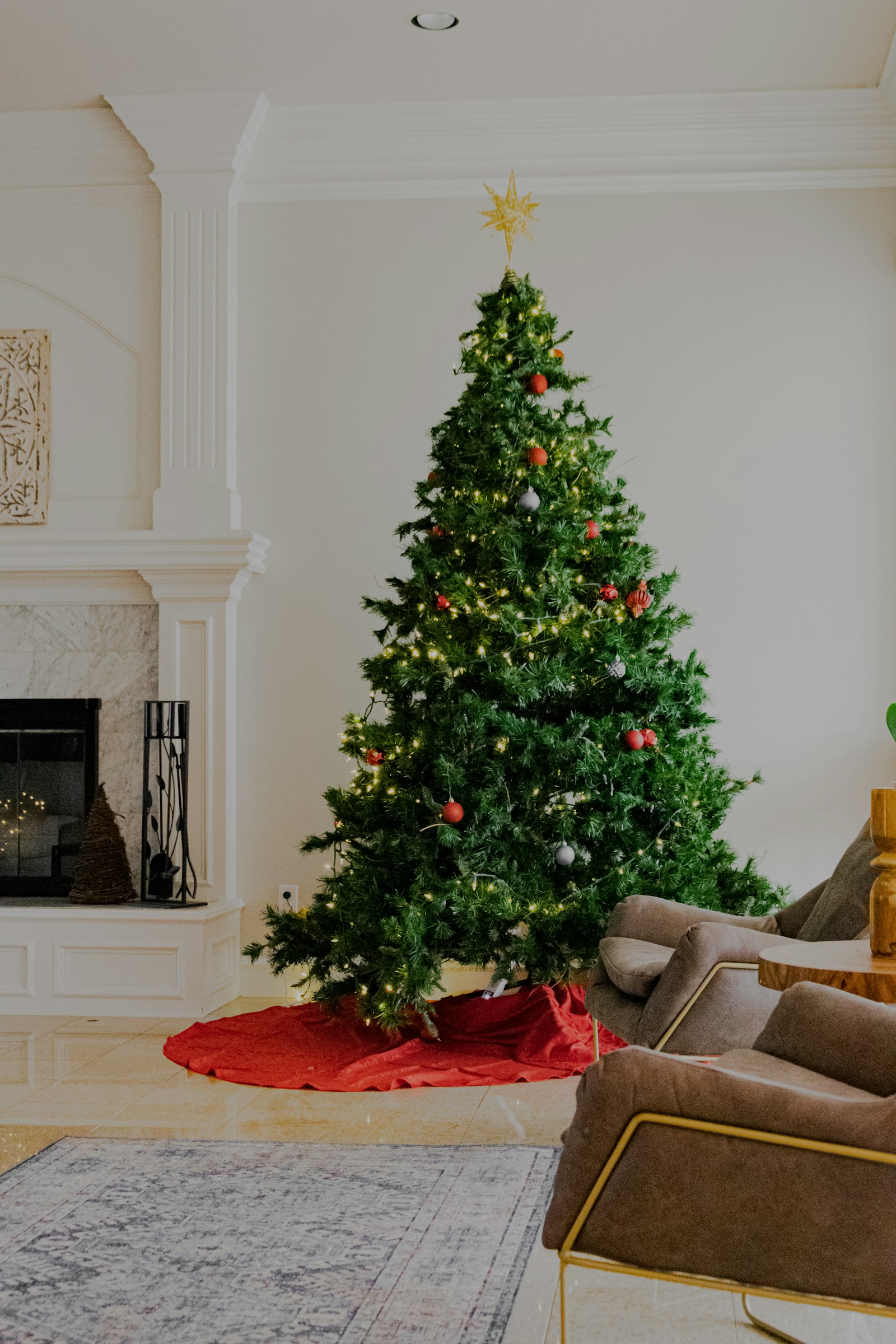 Full green Christmas tree with red ornaments beside a white fireplace