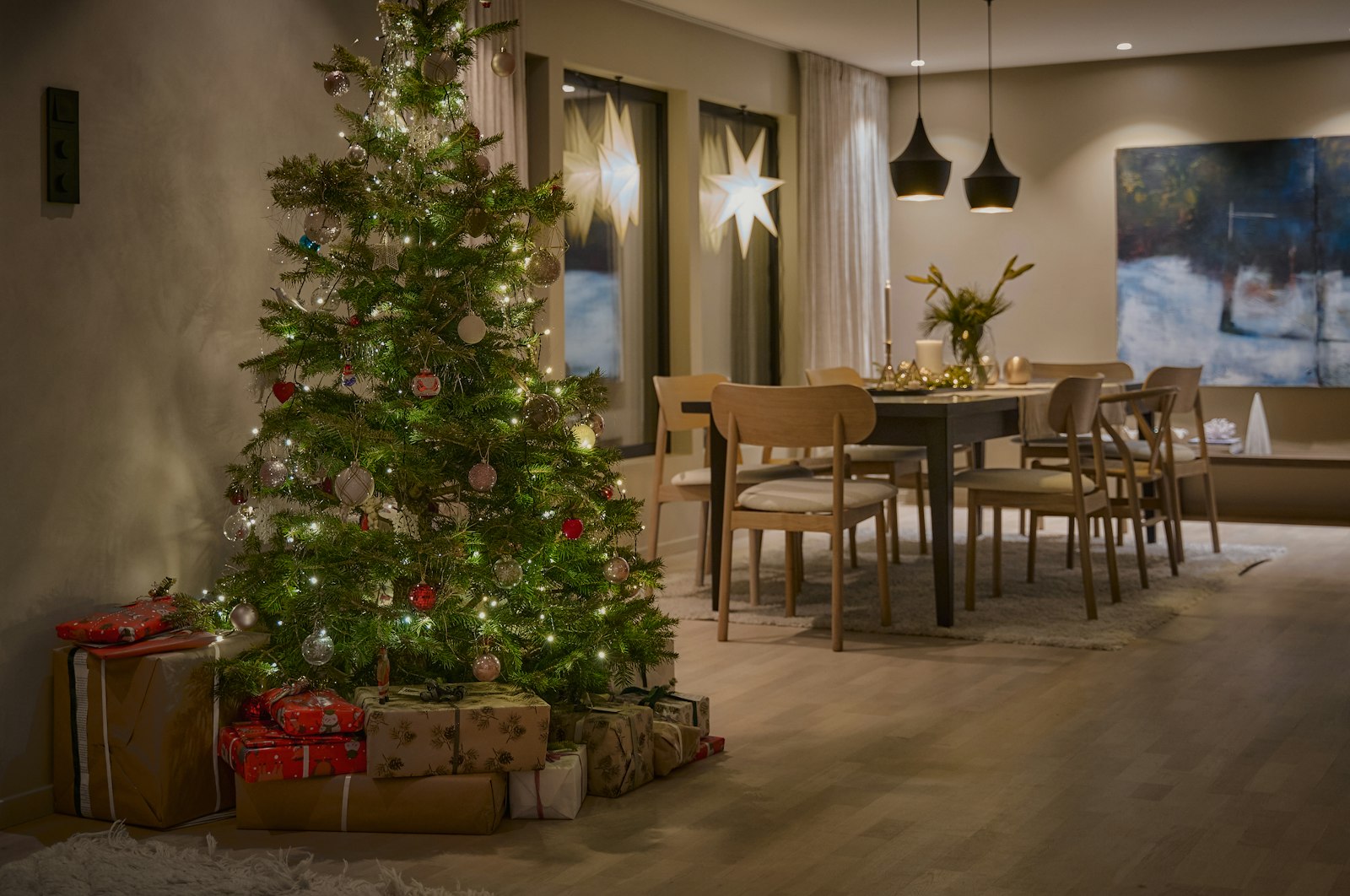 Tall decorated Christmas tree with gifts beside a dining table