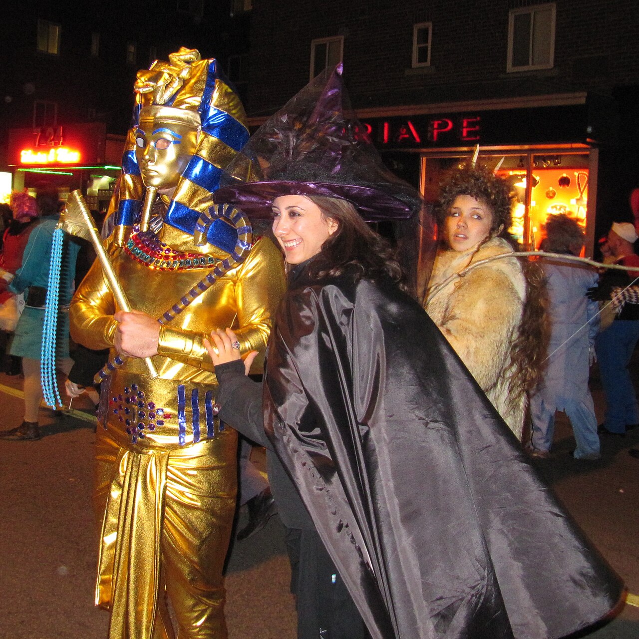 Person in a gold pharaoh costume next to a woman dressed as a witch on Halloween night