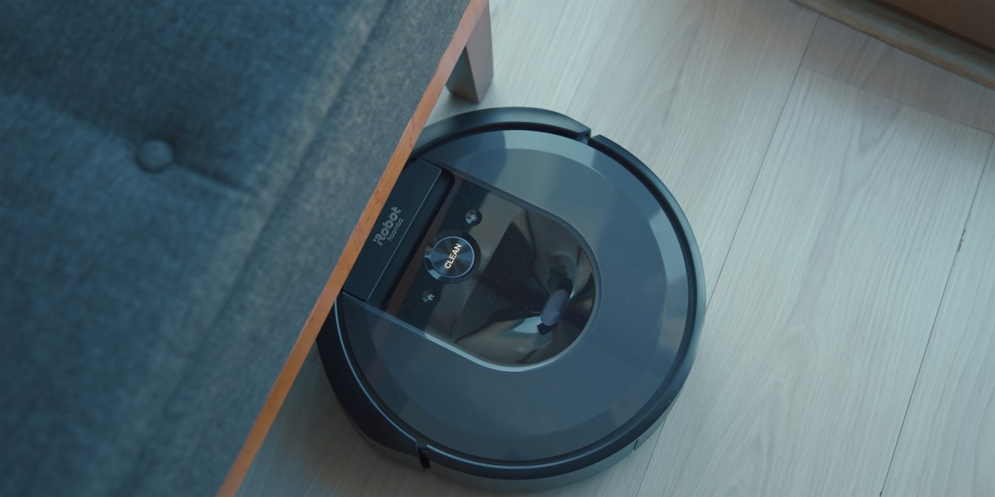 A robot vacuum cleaner gliding along a wood floor beside a sofa