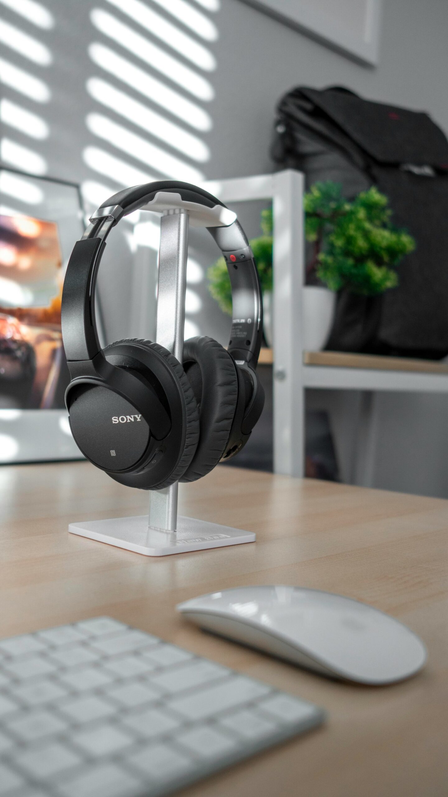 Black Sony over-ear headphones on a desk stand beside a keyboard and mouse