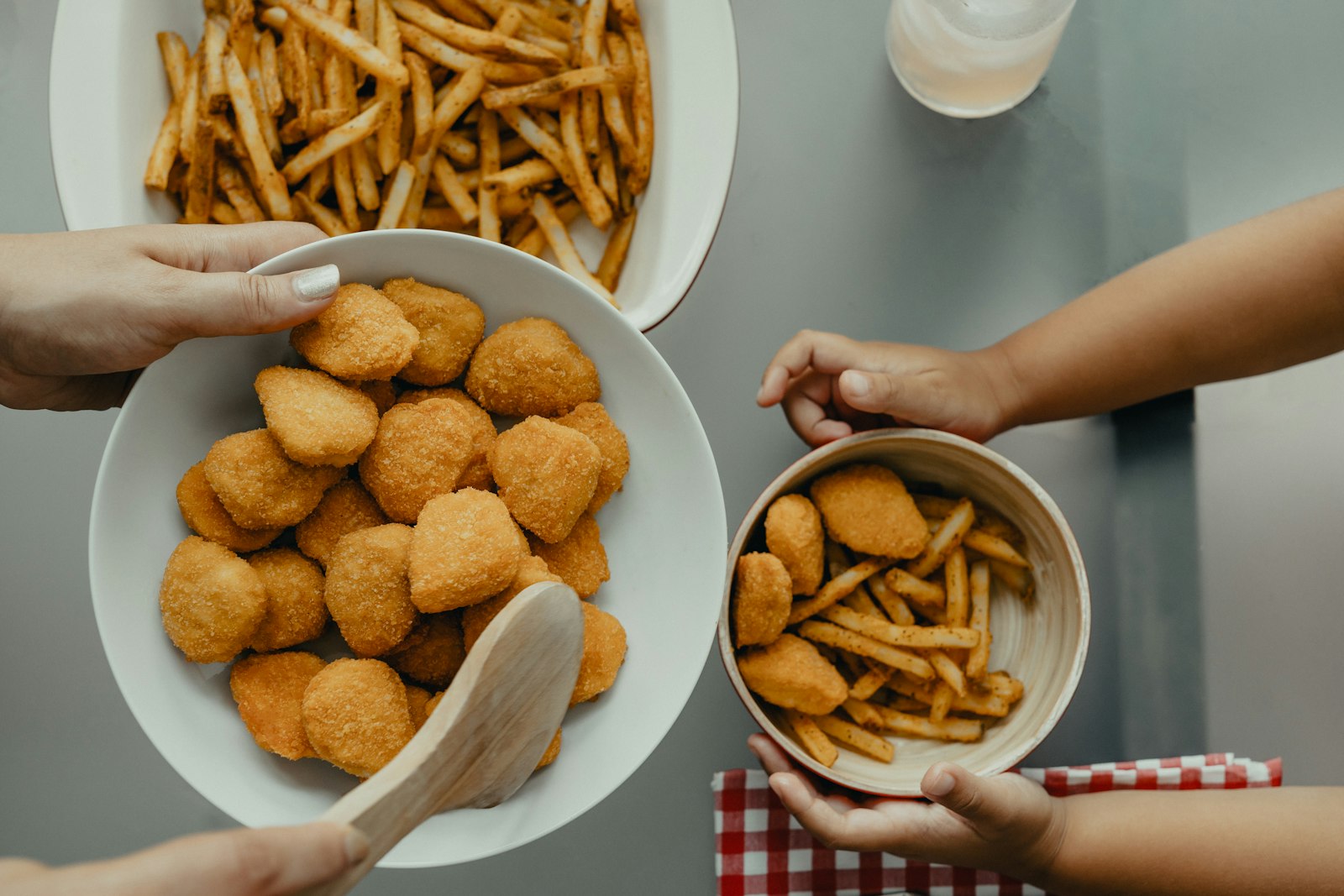 Hands sharing a bowl of crispy nuggets beside a bowl of fries