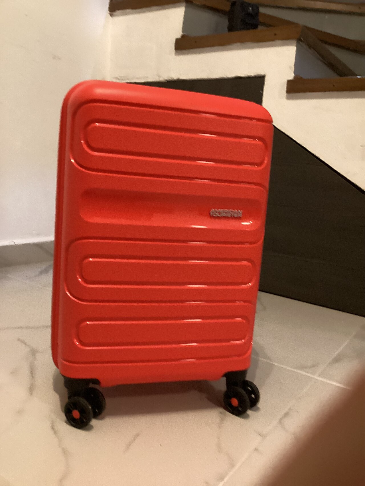 A red American Tourister hardside carry-on spinner suitcase standing on a tile floor