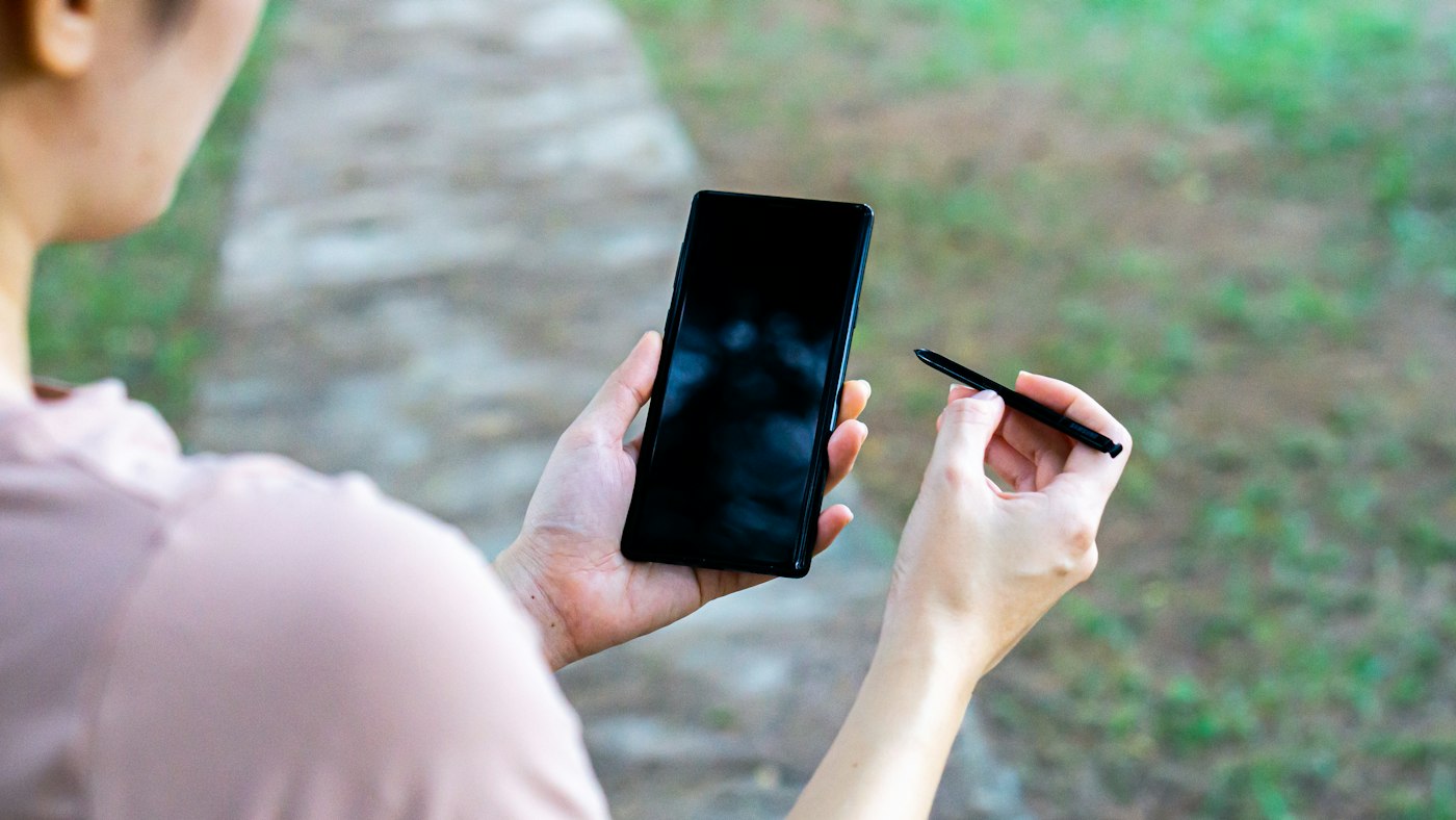 Person holding a black Android smartphone and a stylus pen outdoors