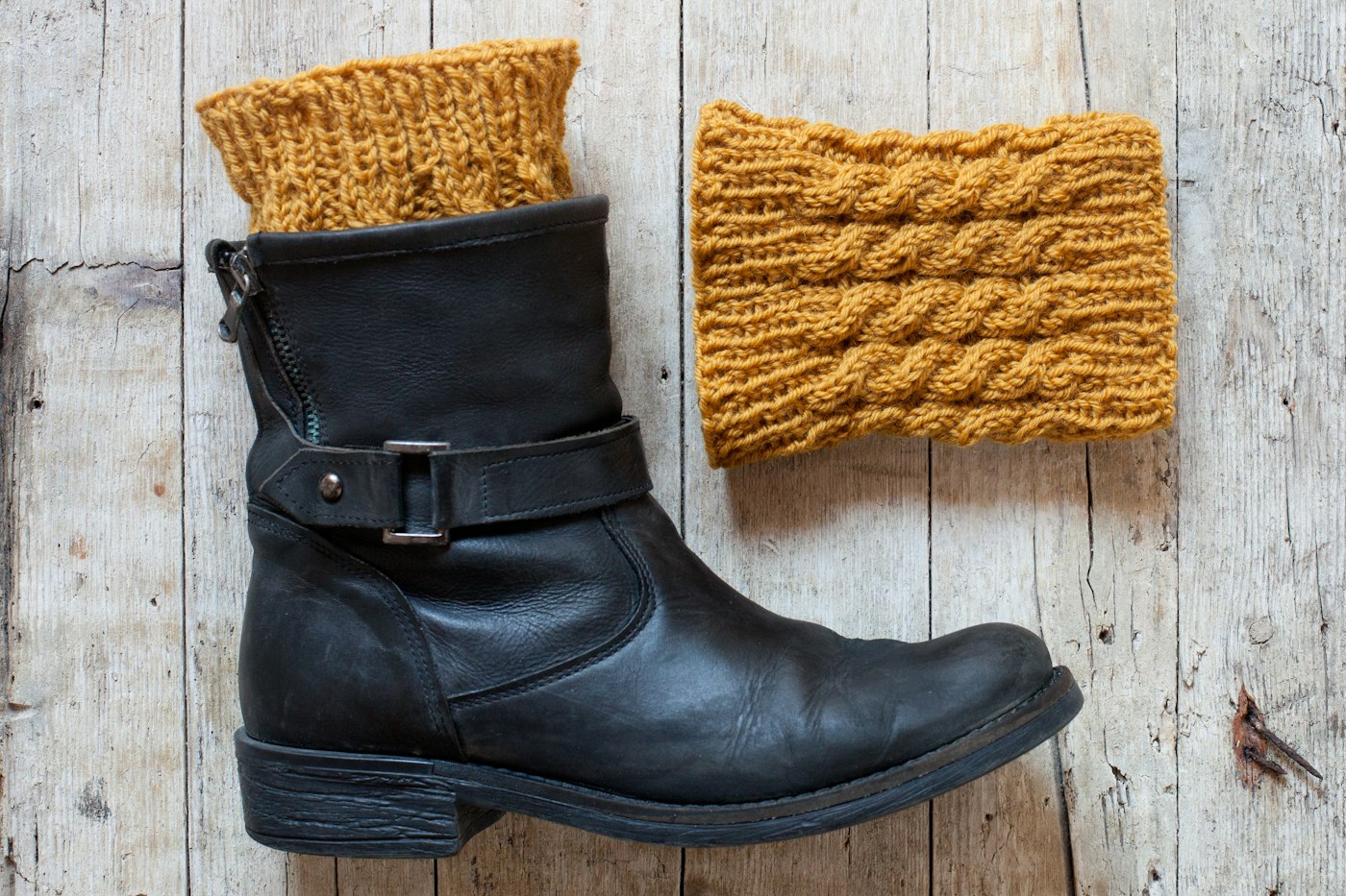 A pair of black boots beside a yellow knitted hat on a winter day