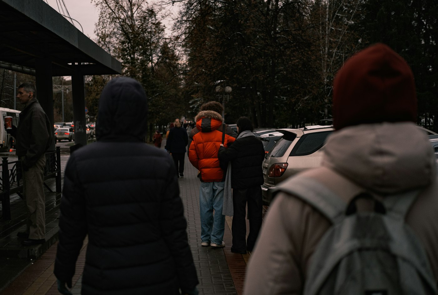 Commuters in jackets walking along a city sidewalk on a cool day