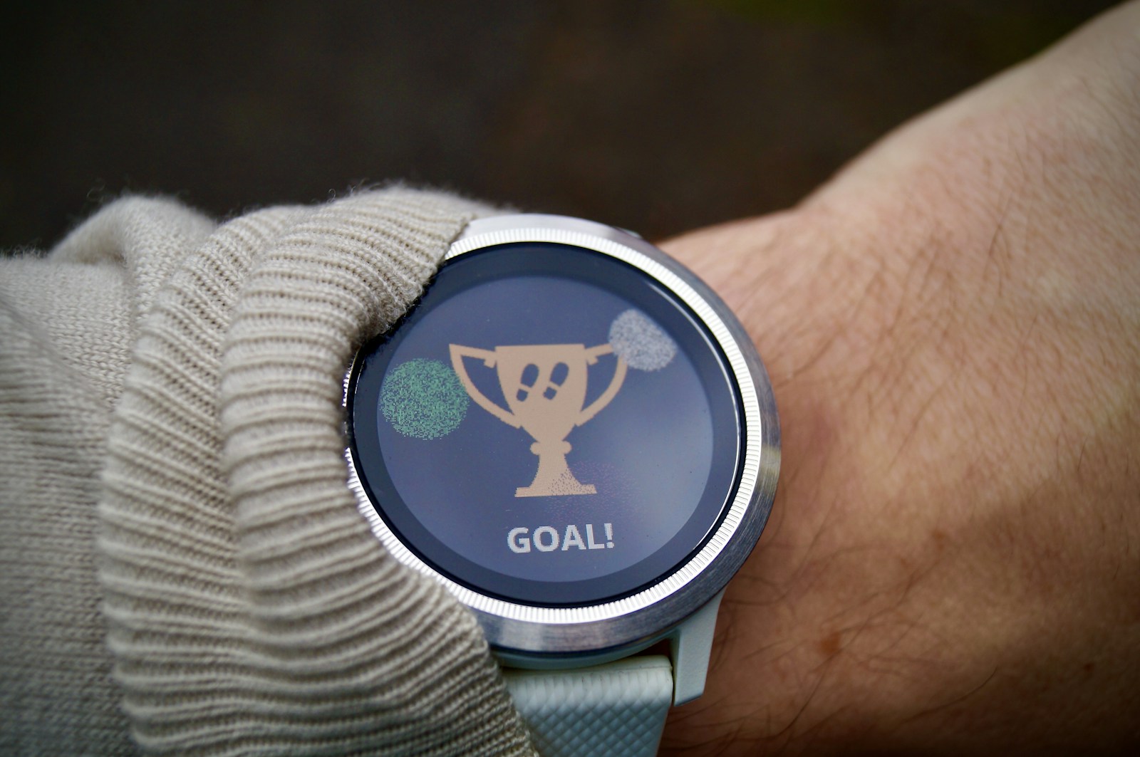 Round fitness watch on a wrist showing a goal-reached trophy screen