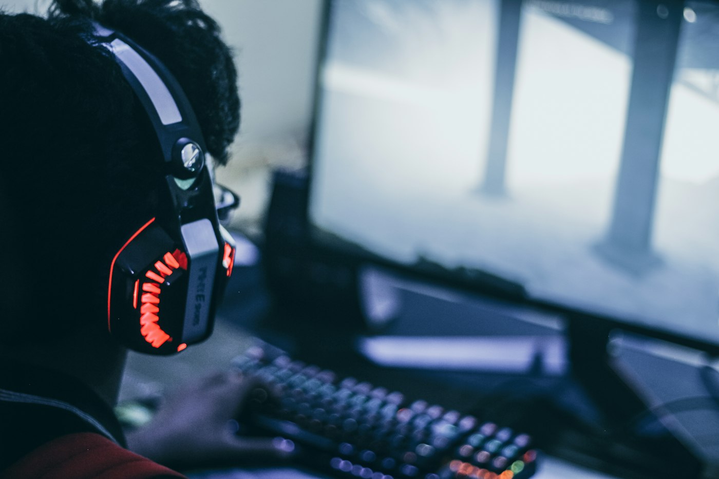 Gamer wearing a lit-up gaming headset at a keyboard and monitor