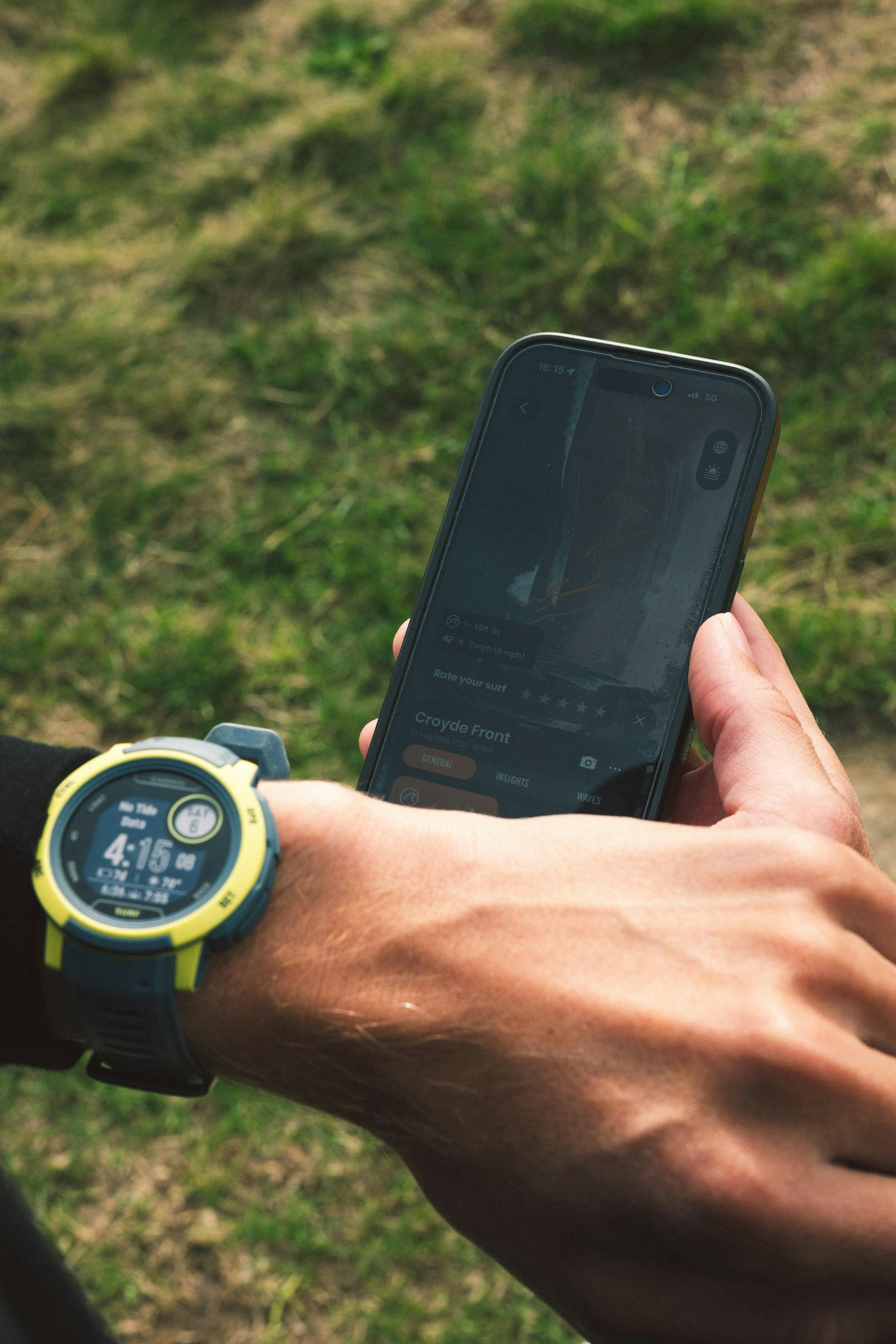 Garmin Instinct rugged smartwatch on a wrist while the wearer checks a phone outdoors