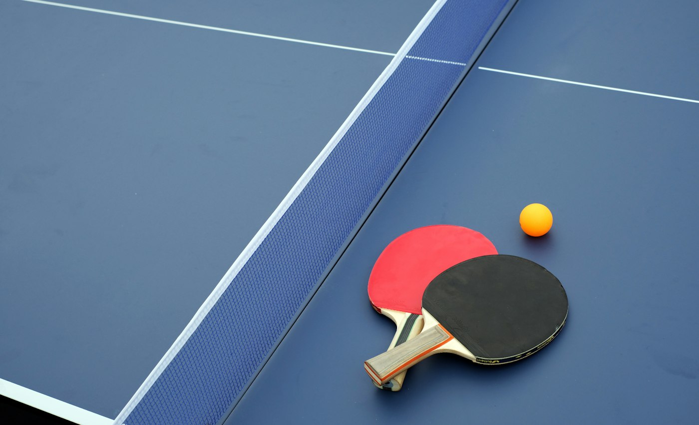 Two ping pong paddles and a ball on a blue table
