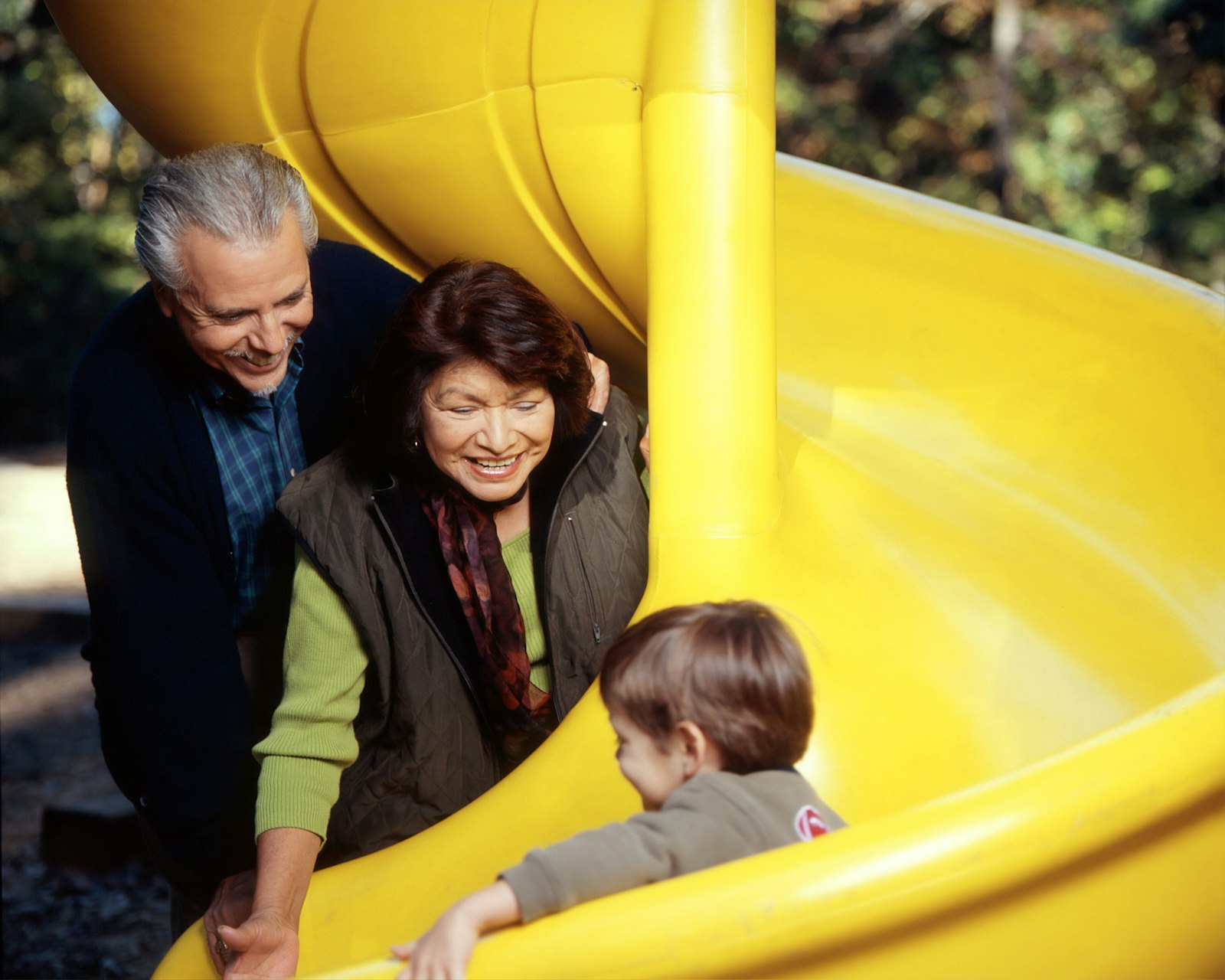 Grandparents watching a young child come down a yellow playground slide