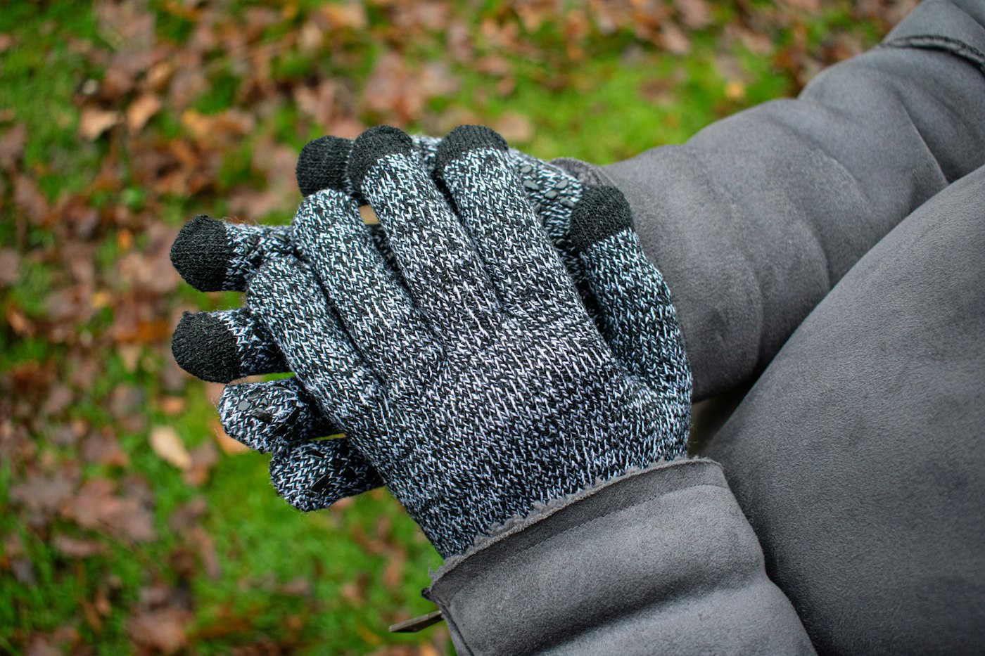 Gloved hands in grey knit gloves with touchscreen fingertips on a cold fall day