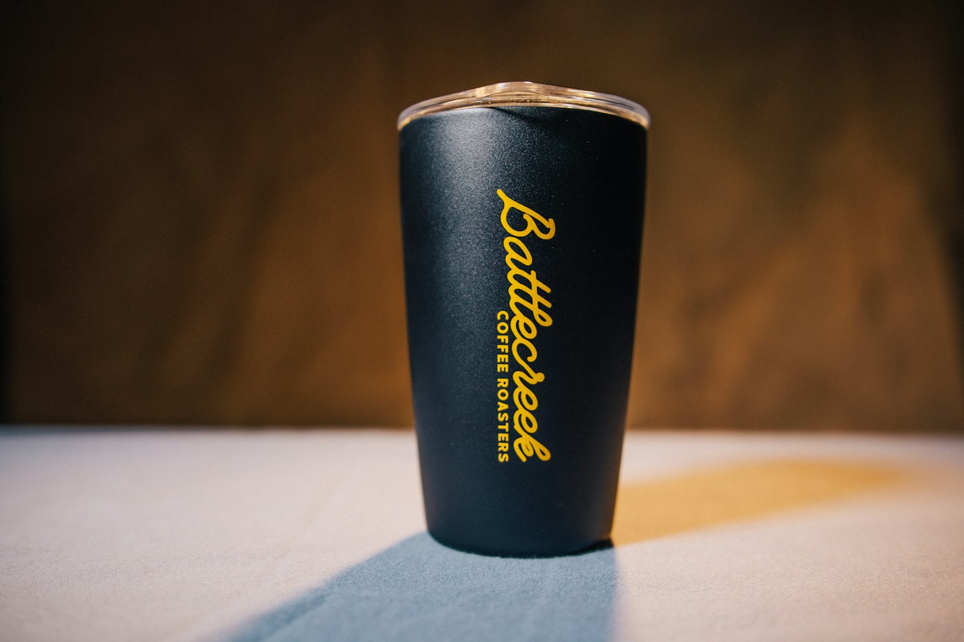 Black insulated stainless steel tumbler with a clear lid on a table