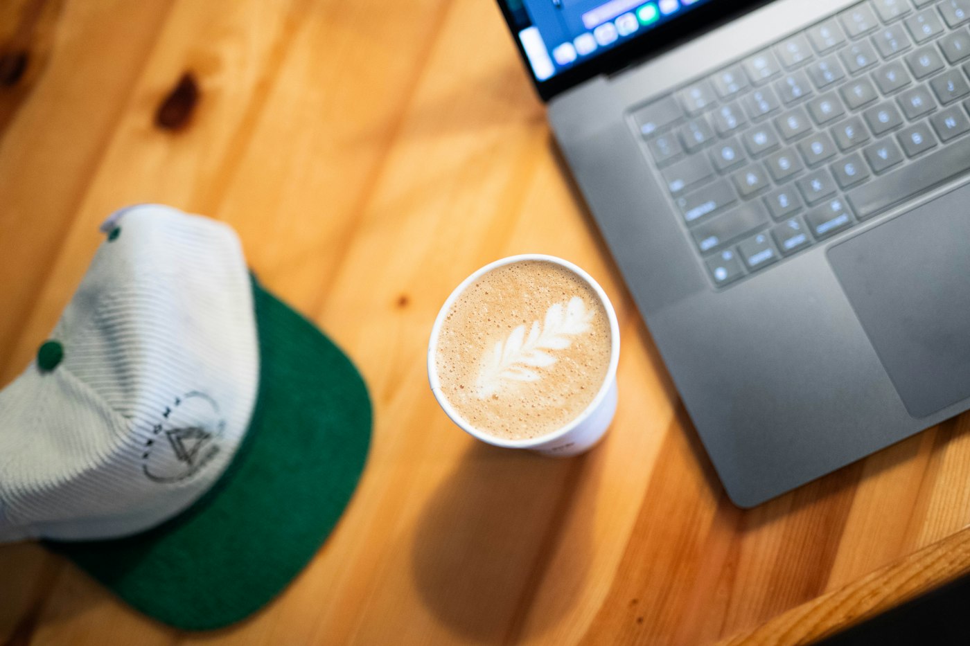 Person working on a laptop beside a latte at a cafe
