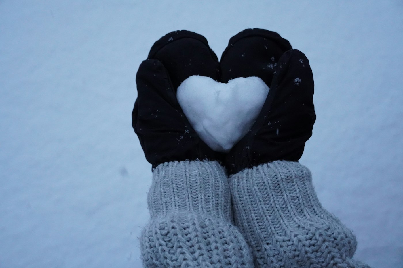 Two mittened hands holding a heart shaped piece of snow