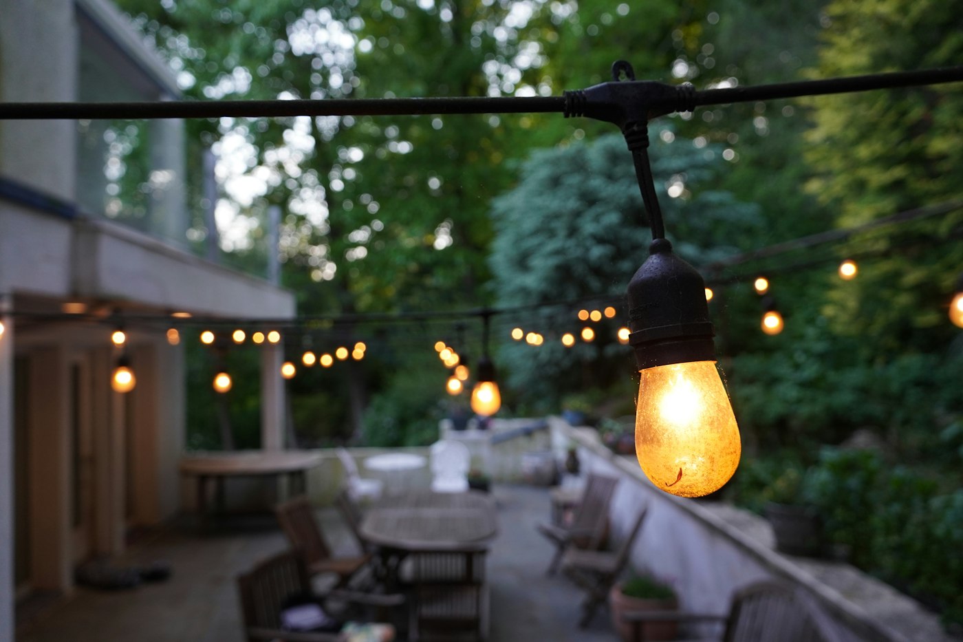 Outdoor string lights glowing over a patio with tables and chairs