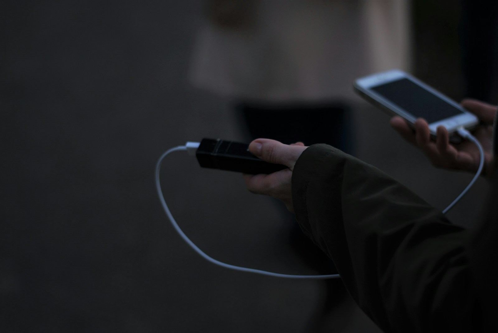 Person holding a phone connected by cable to a small portable charger