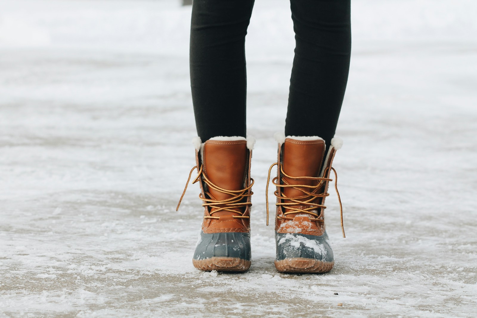 Brown and grey lace-up duck-style winter boots on slushy pavement