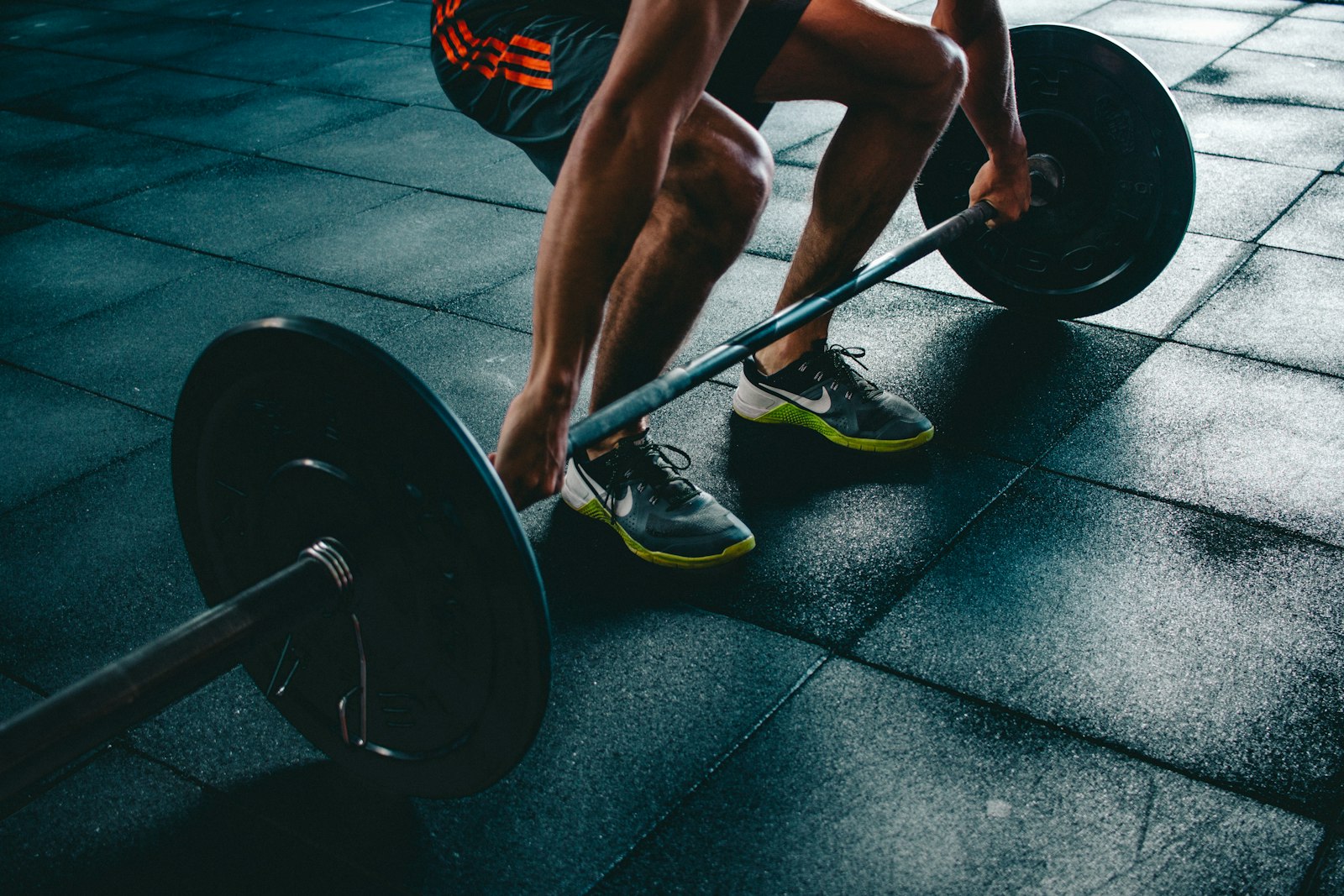 Athlete about to lift a barbell in a gym, the kind of training where a massage gun is used for recovery