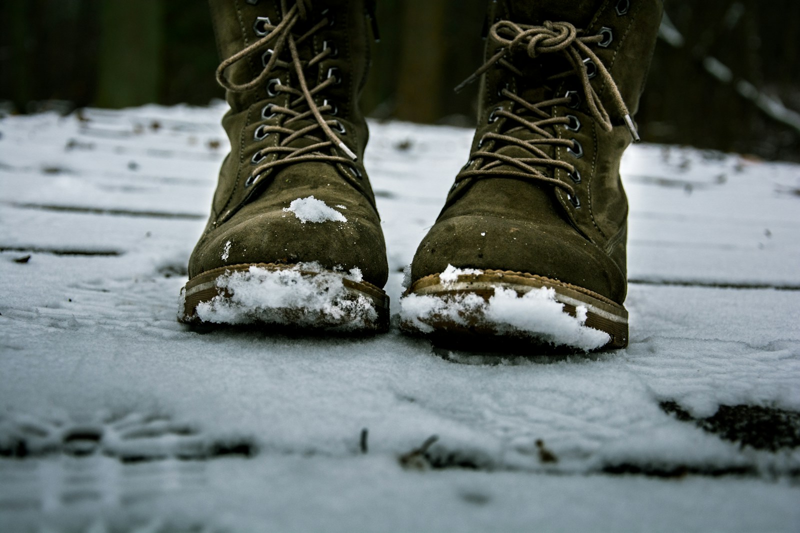 Olive lace-up boots with snow packed on the soles