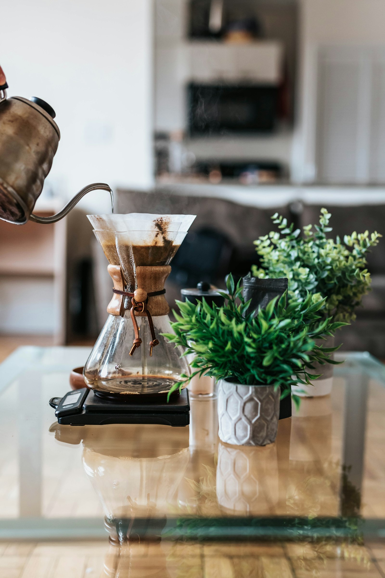 Gooseneck kettle pouring hot water over coffee in a glass pour-over server