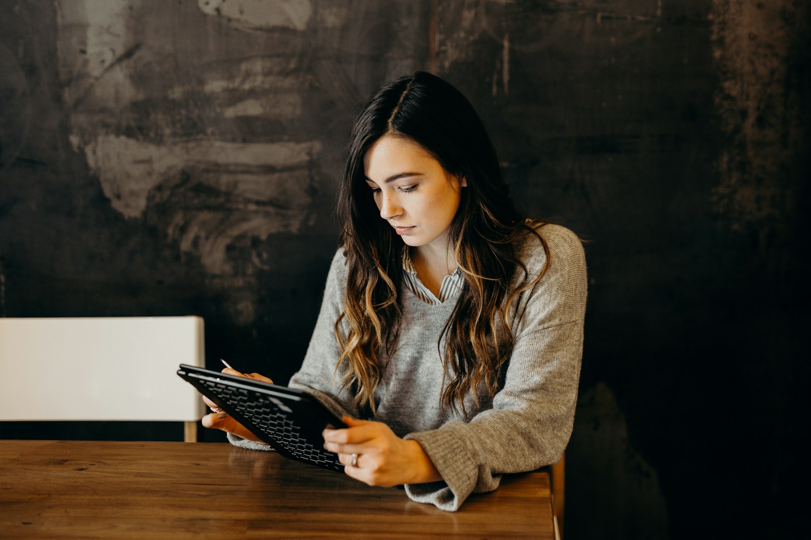 Woman in a grey sweater using a tablet at a wooden table