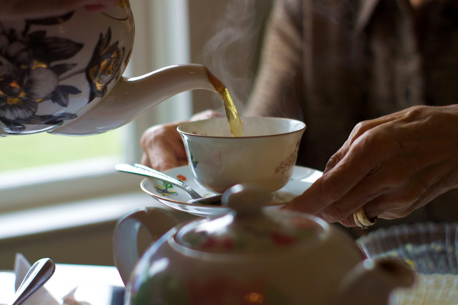 Hot tea being poured from a teapot into a white teacup
