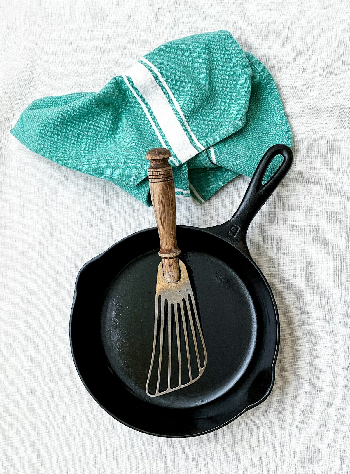 Seasoned cast iron skillet with a fish spatula and a green tea towel