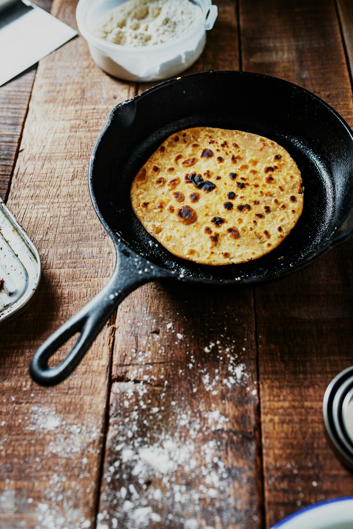 Cast iron skillet with a freshly cooked flatbread on a wooden table