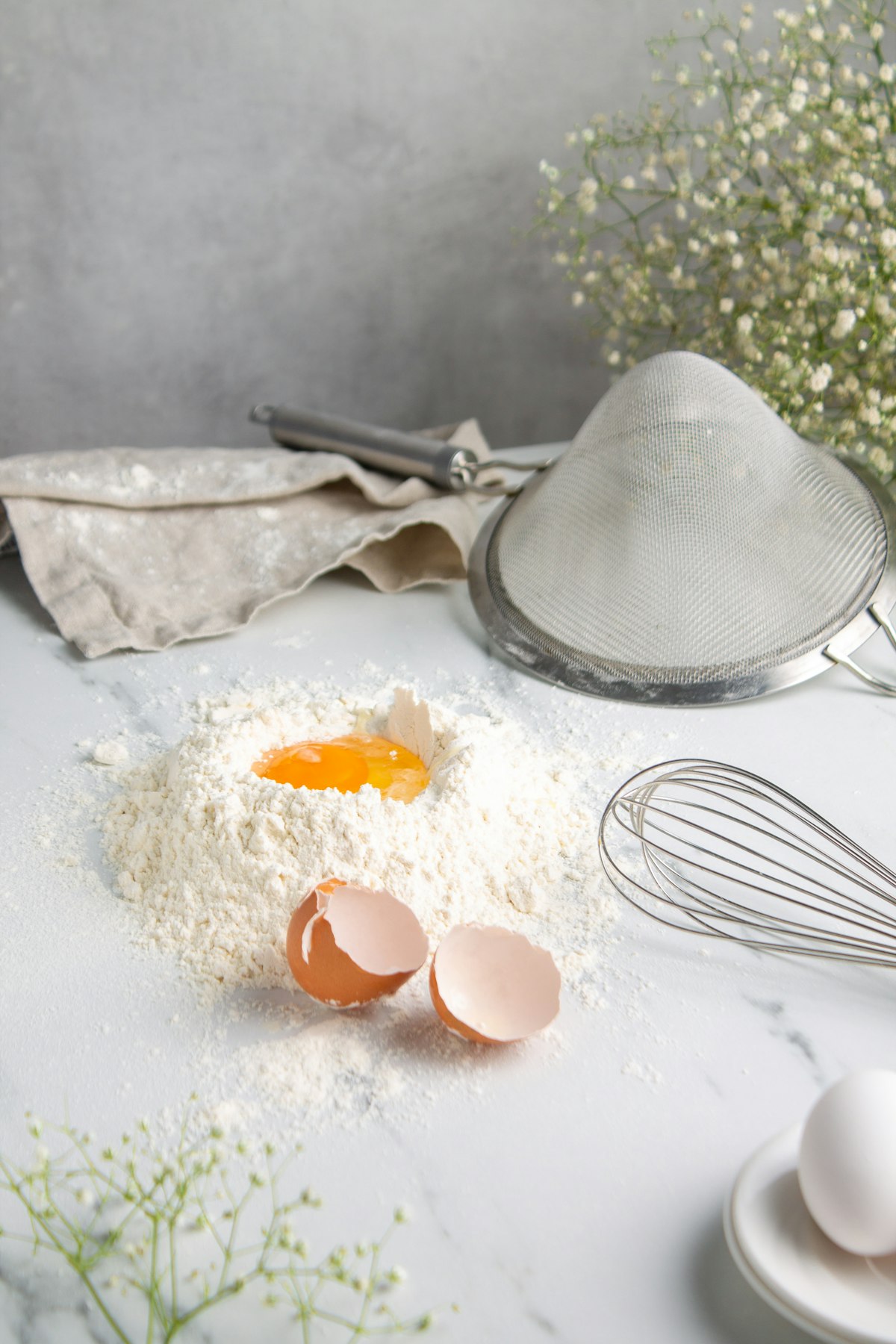 Flour, cracked eggs, a whisk and a sieve on a marble counter