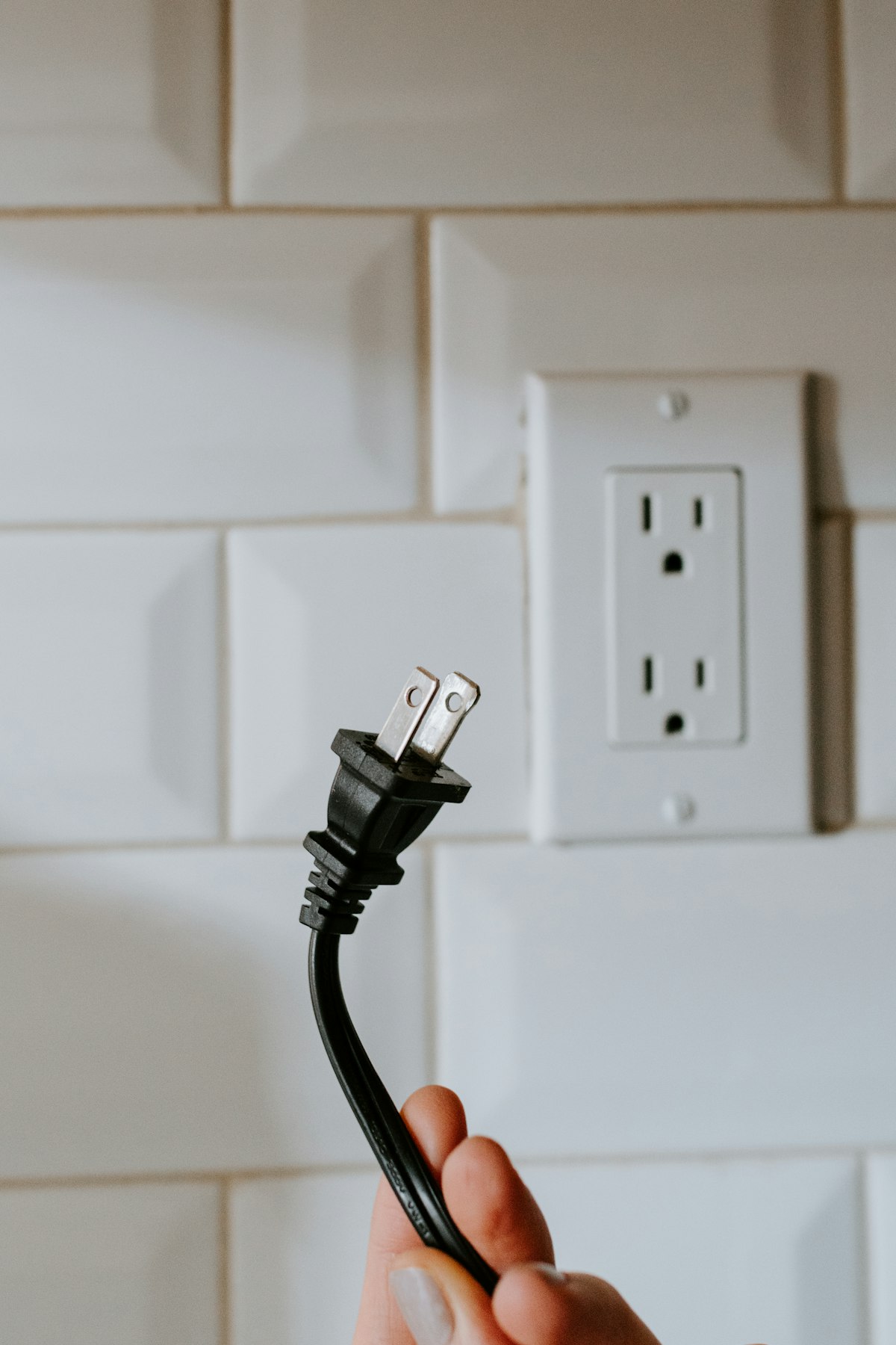 Black power cord beside a wall outlet