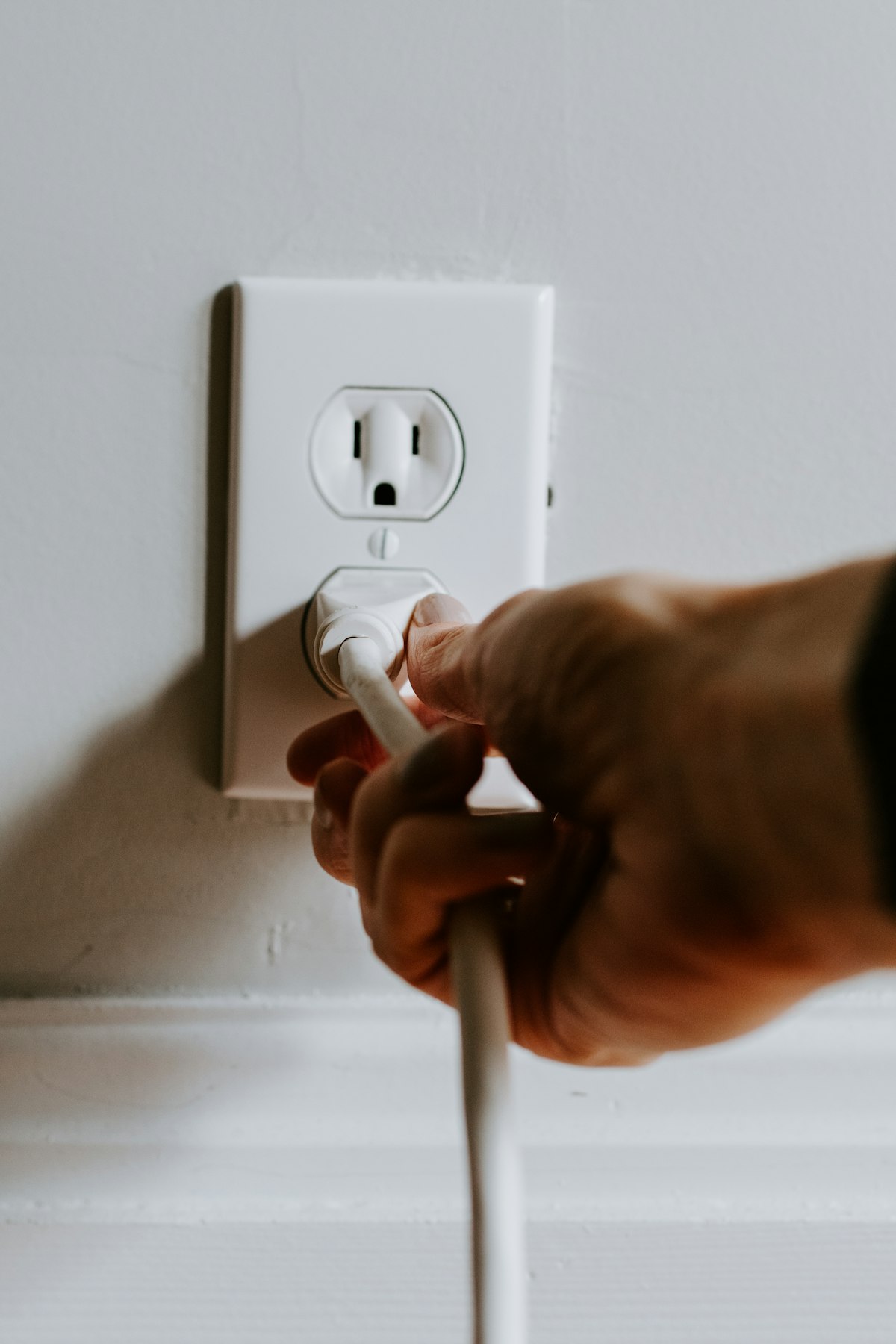 Hand plugging a white cord into a wall outlet