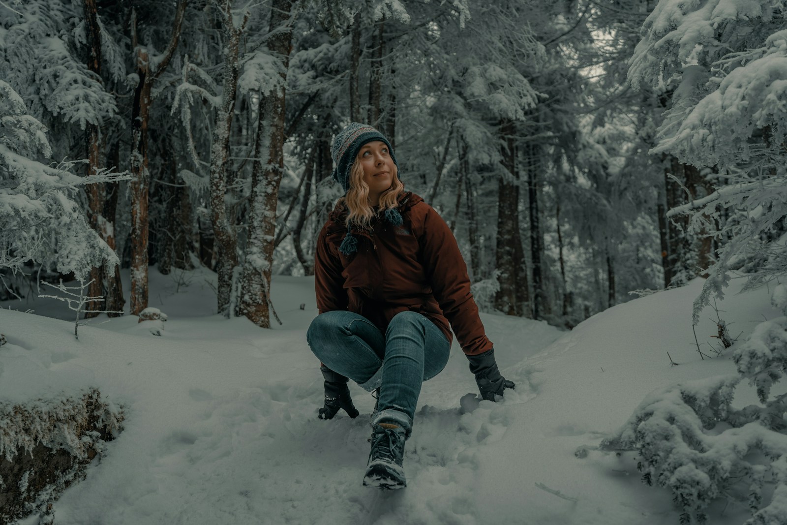 Woman crouching on a snowy forest trail in winter boots