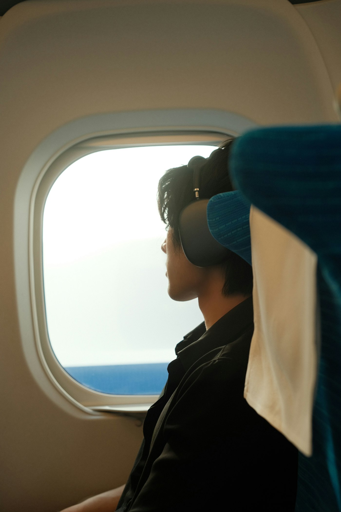 Traveller wearing over-ear noise-cancelling headphones beside an airplane window