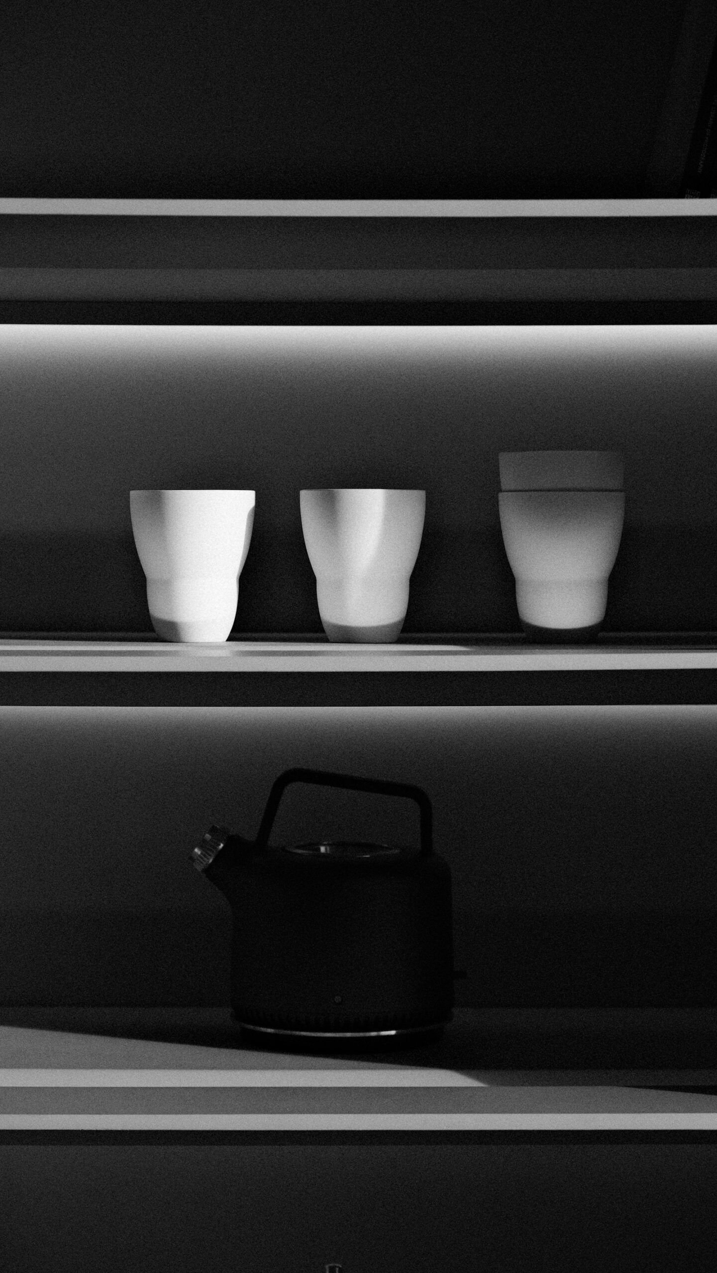 Compact black kettle and white cups on lit kitchen shelves