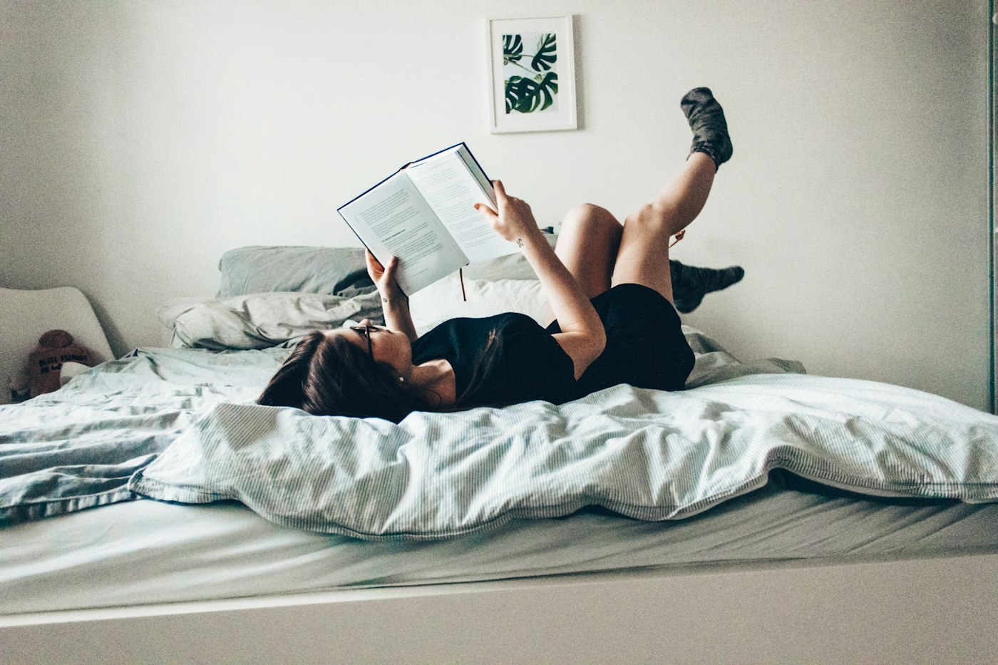 Woman lying on a bed reading a book with her legs in the air