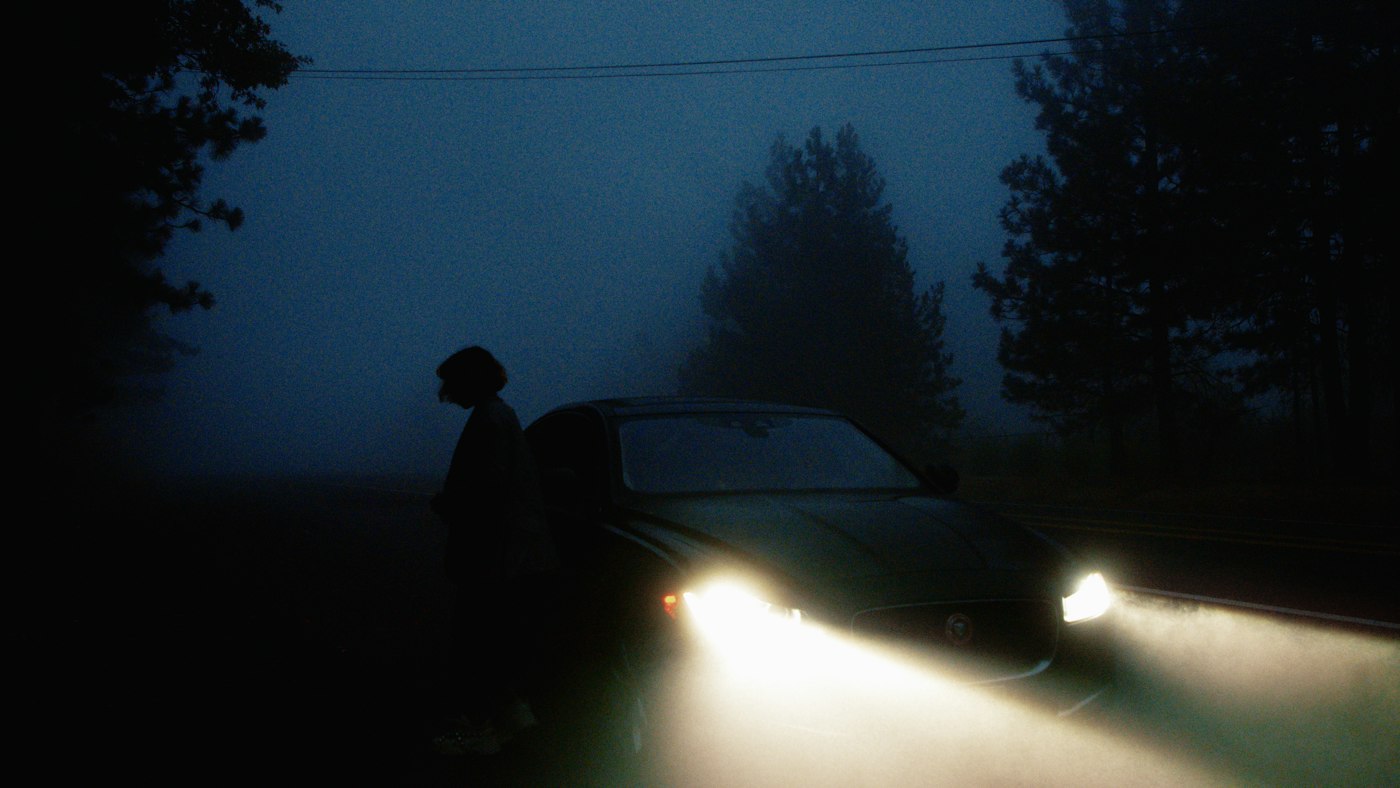 A person standing beside a car in foggy darkness on a roadside