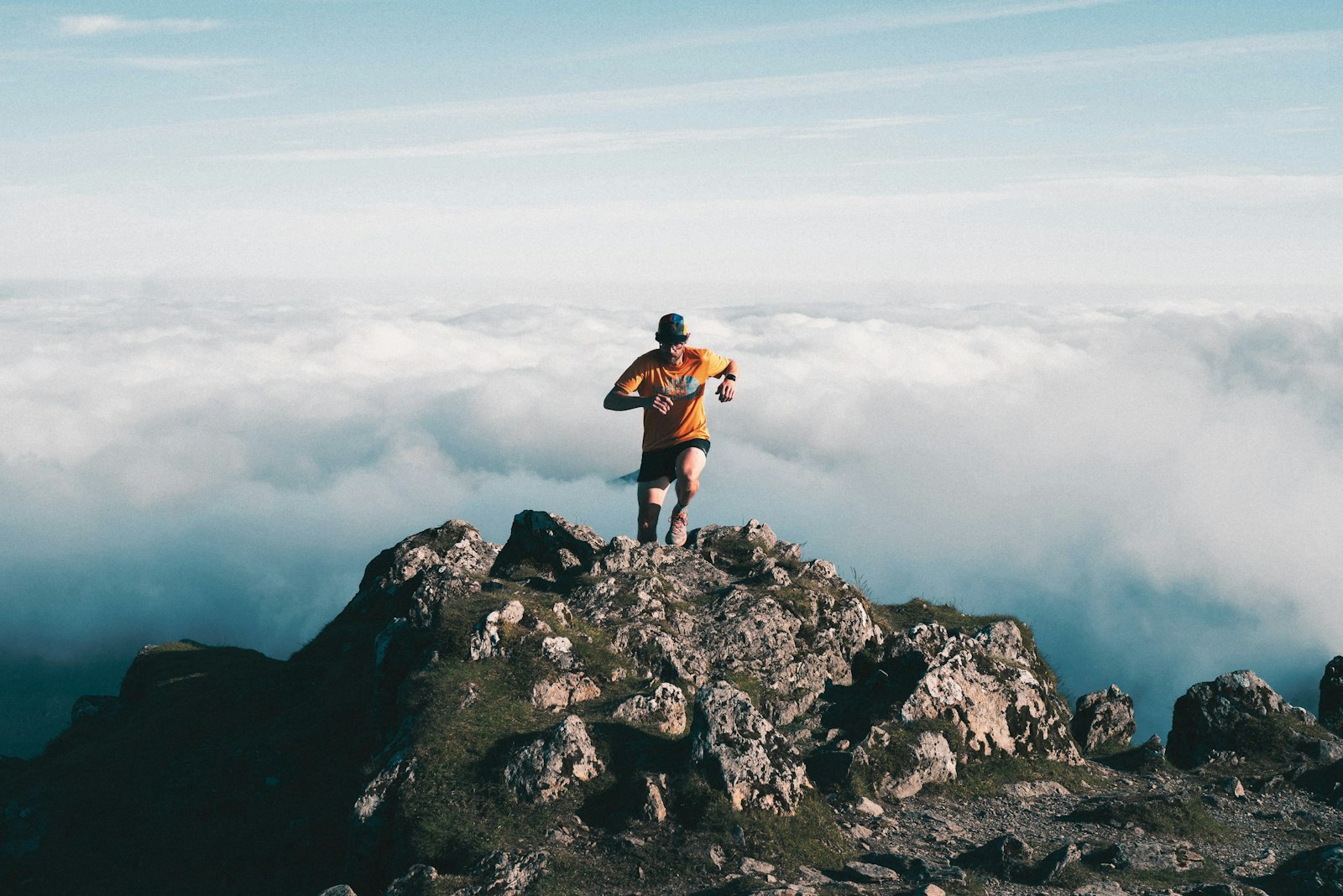 Runner on a rocky mountain peak above the clouds, the kind of route a multisport GPS watch tracks