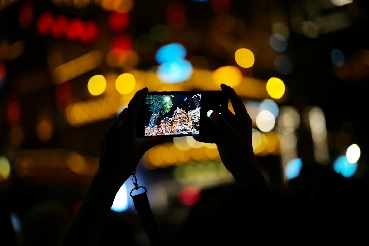 Hands holding up a smartphone to film a brightly lit crowd scene at night