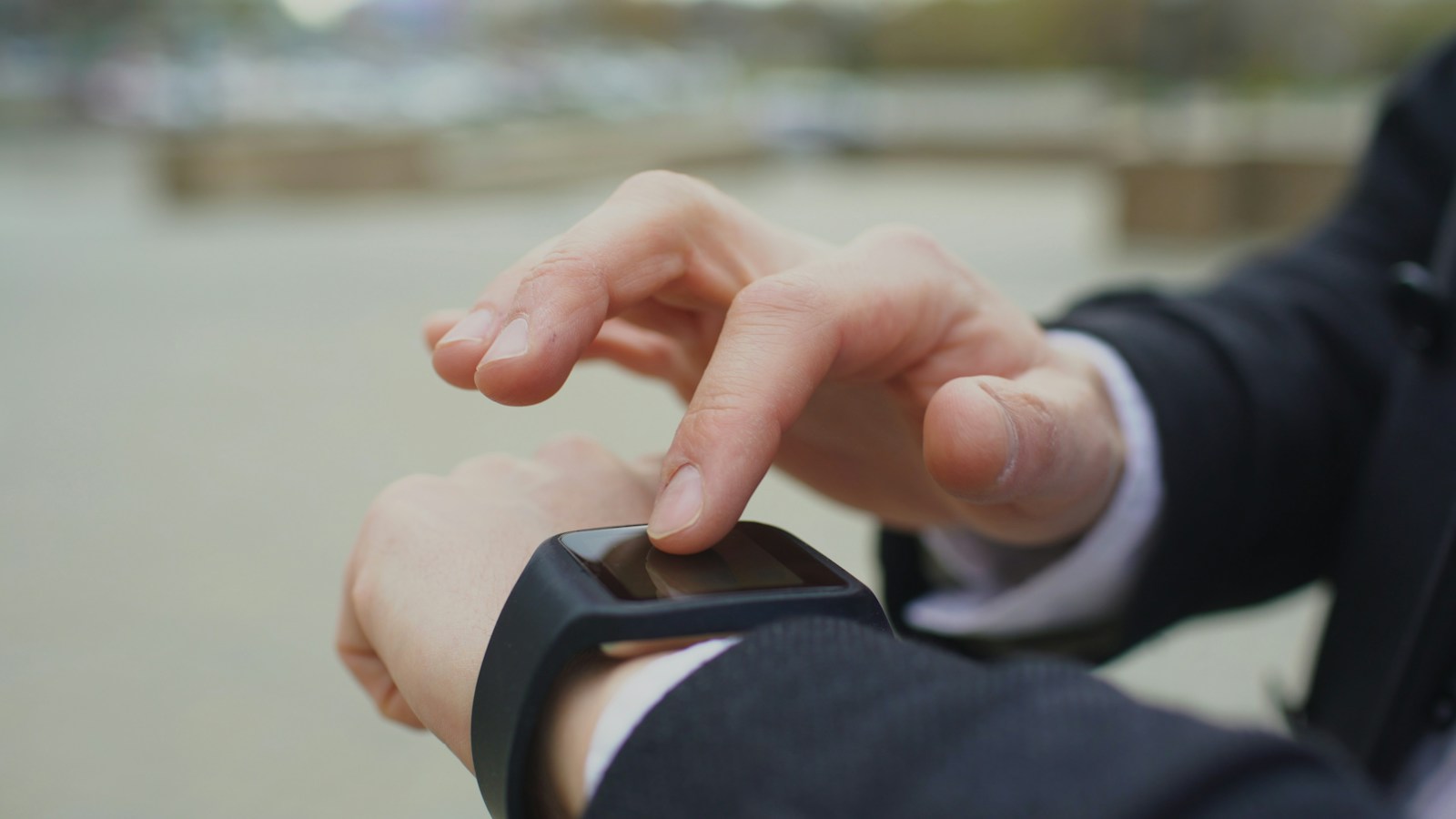 Person tapping the touchscreen of a black smartwatch outdoors