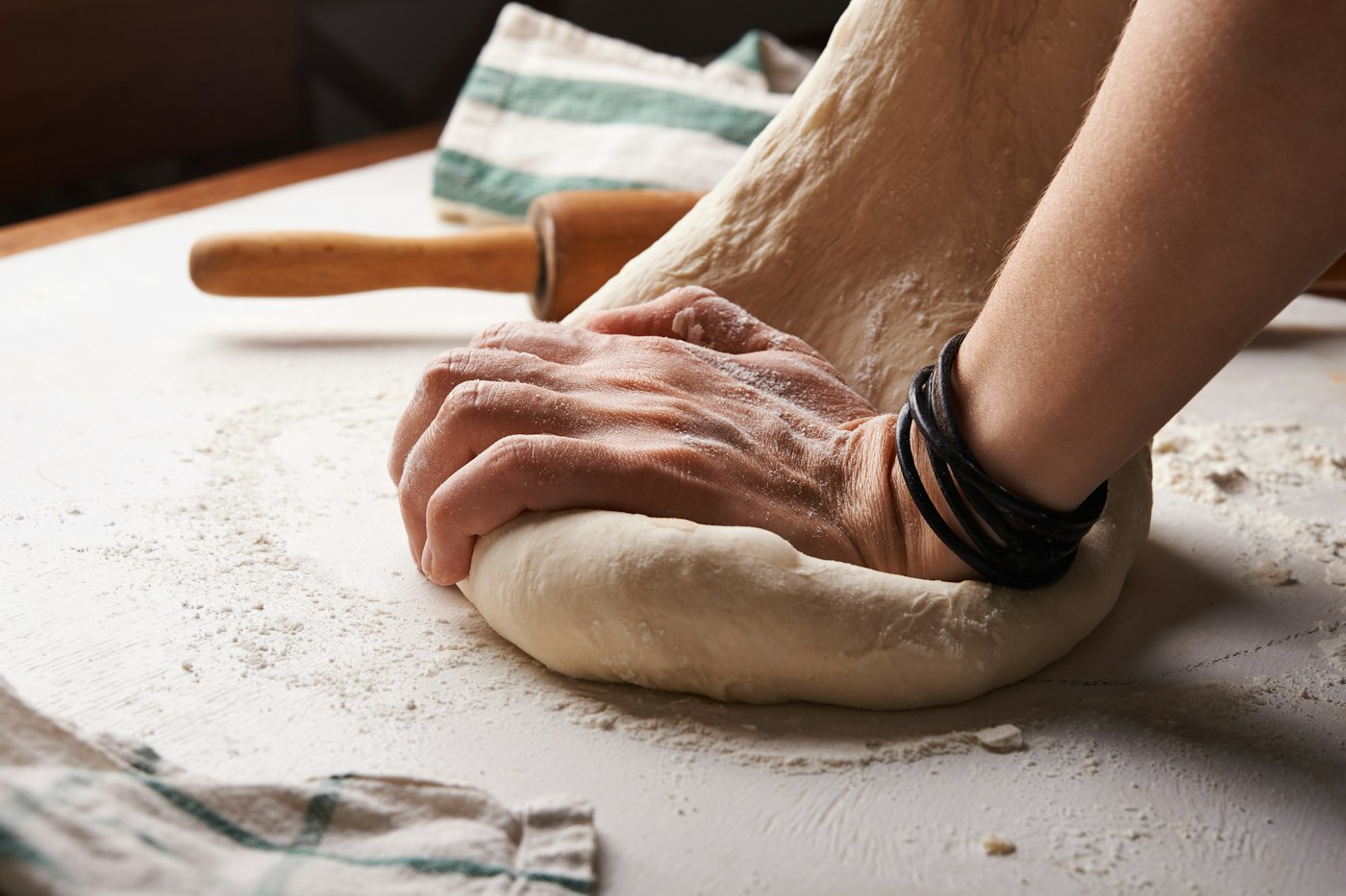 Hands working bread dough on a floured counter