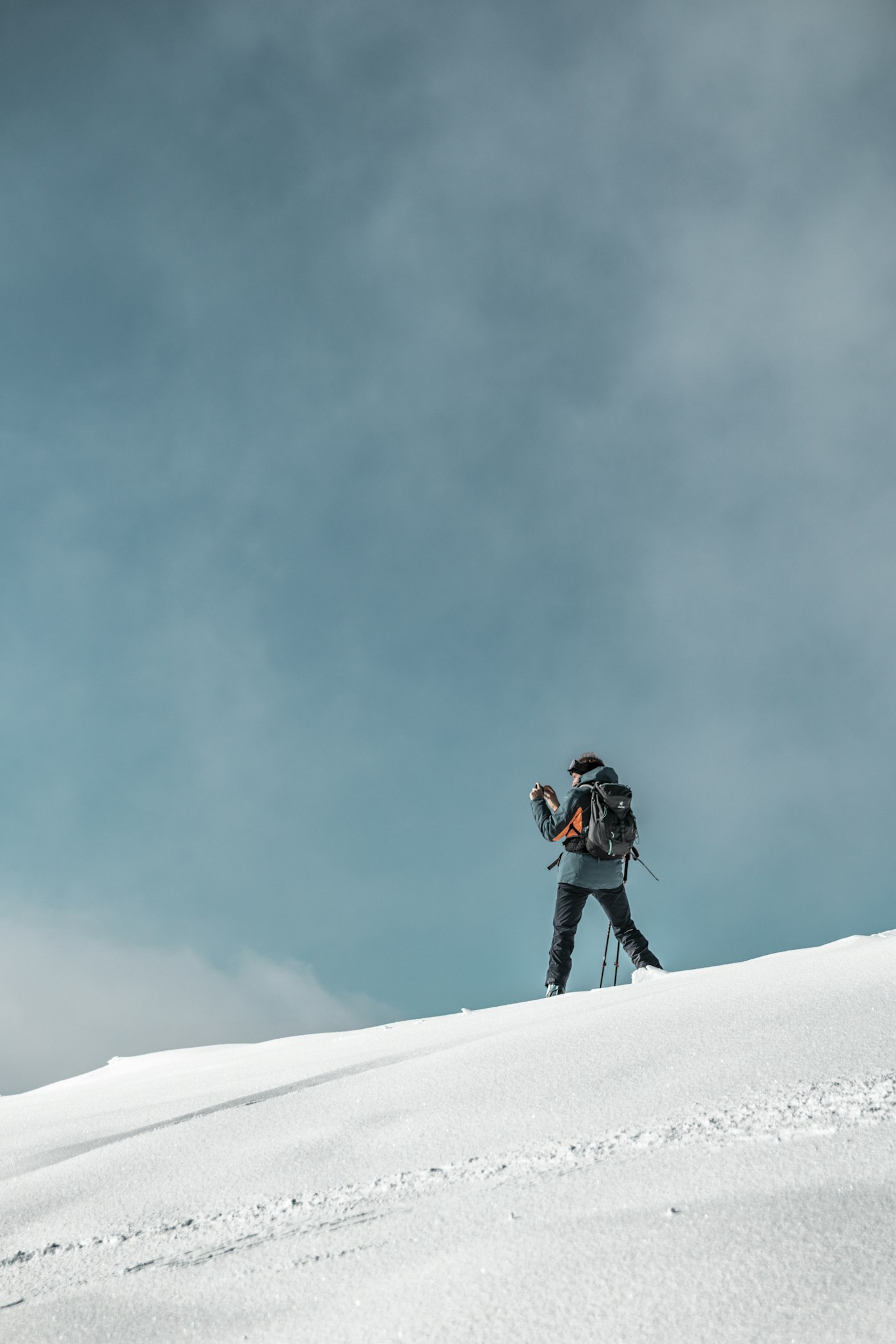 Person with a backpack stands on a snowy slope under a cloudy blue sky