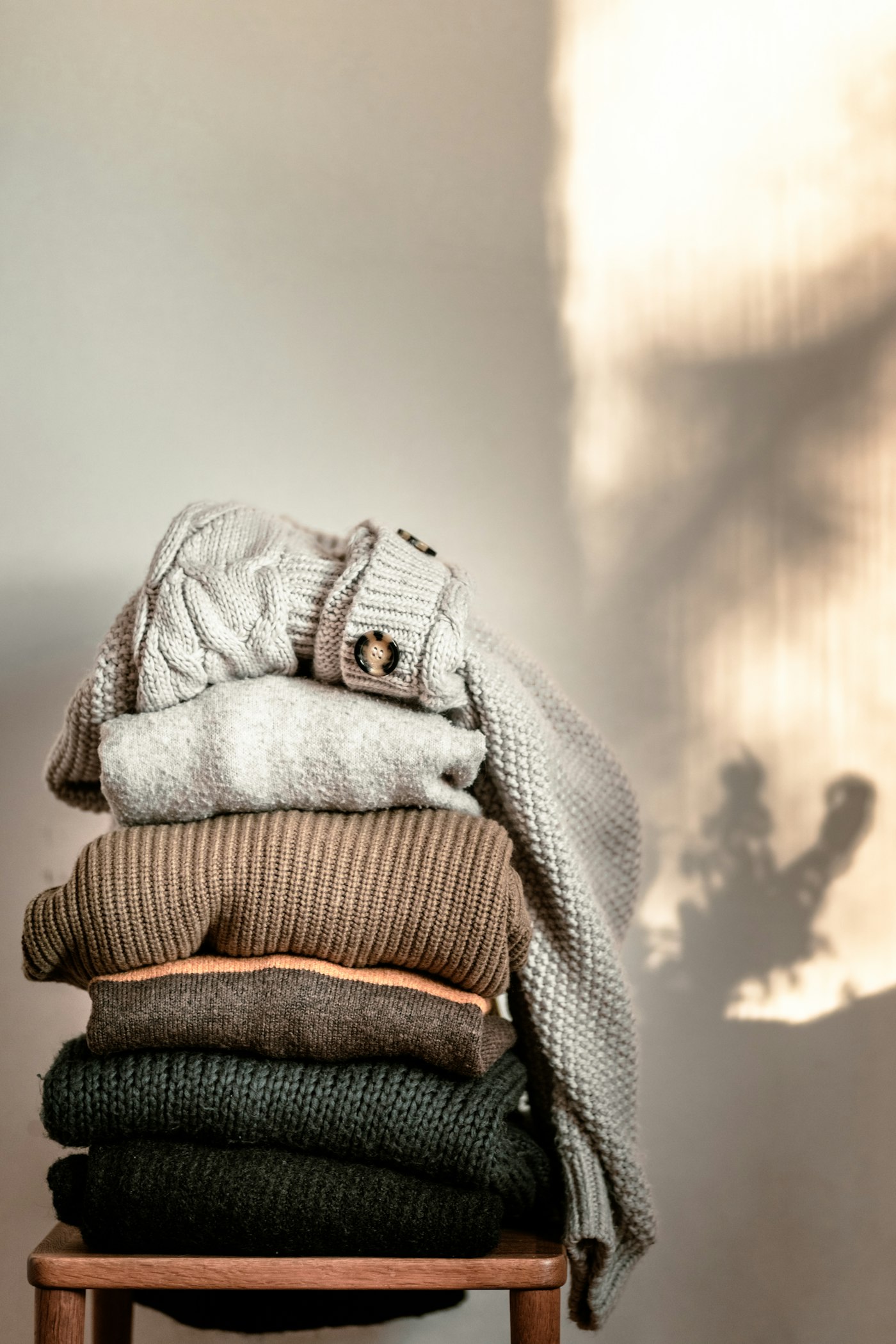 Stack of folded knit sweaters on a wooden stool, showing layered winter clothing