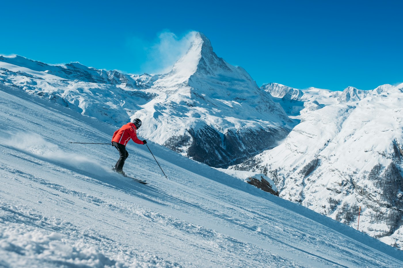 Skier in a red jacket on a sunny alpine slope, an active day that calls for moisture-wicking base layers