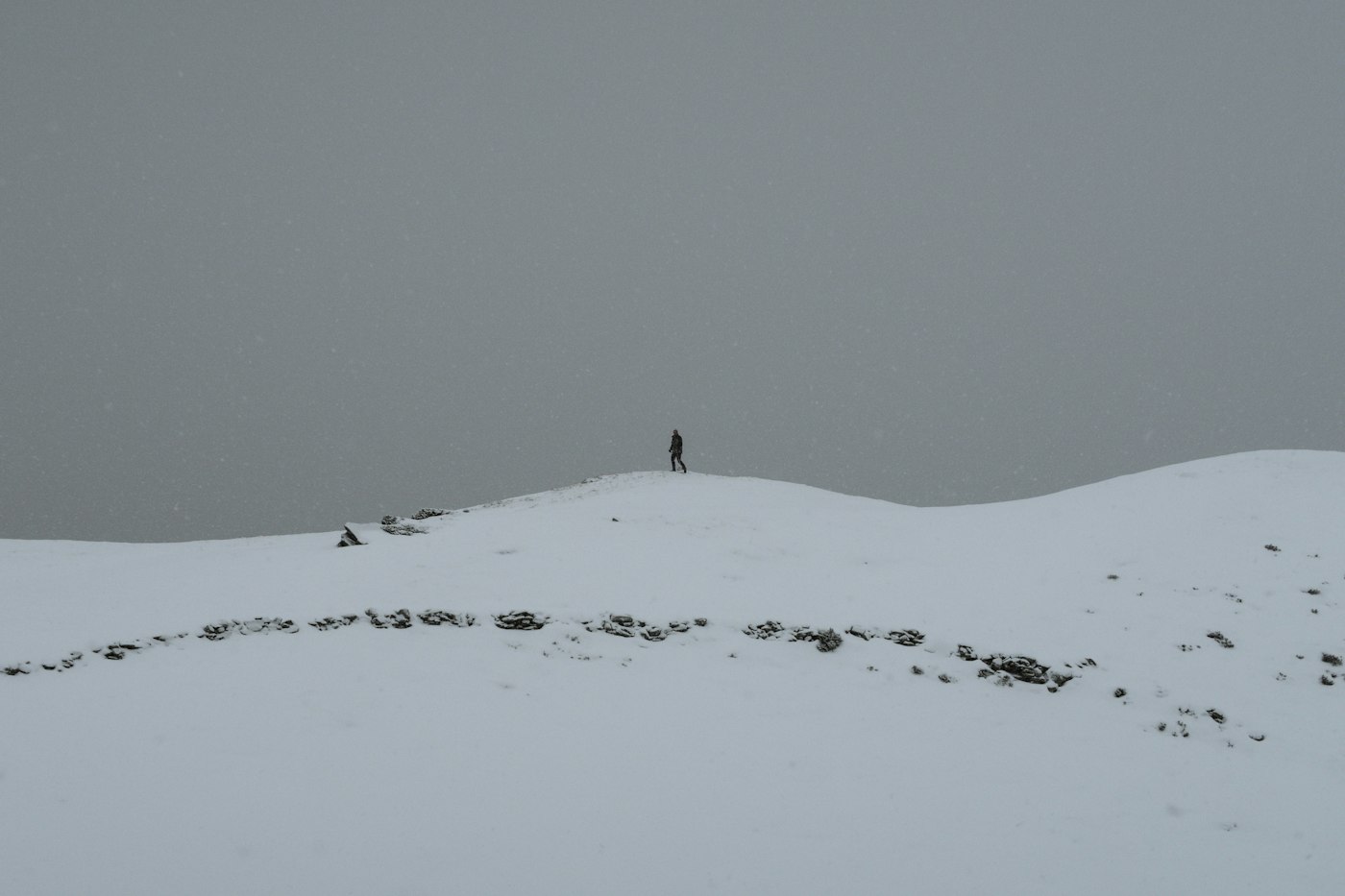 Lone walker on a snow-covered hill under a grey winter sky