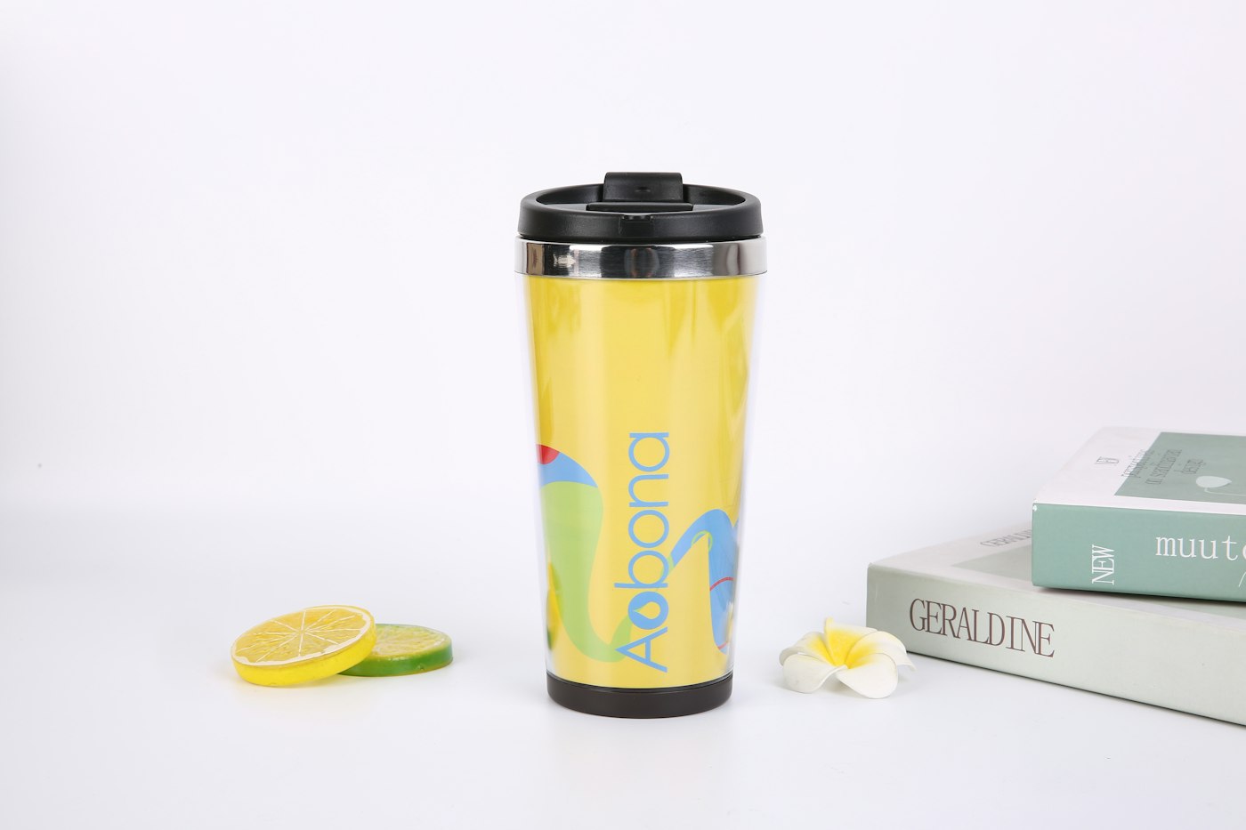 Yellow travel mug with a black lid beside books and a lemon slice