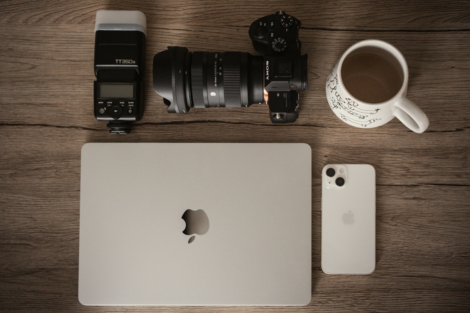 Laptop, phone, camera and coffee laid out on a wooden table