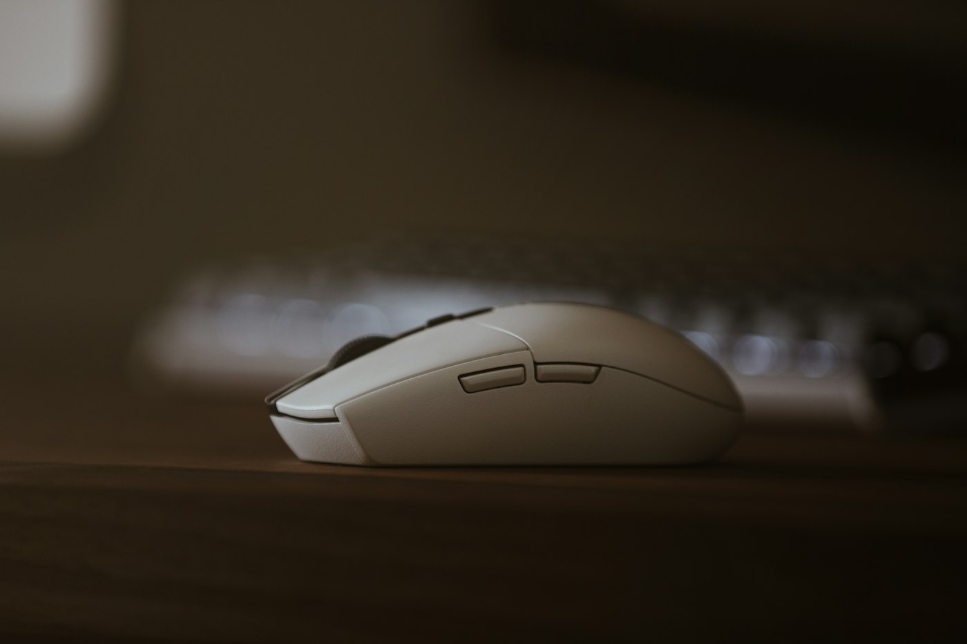 White wireless mouse on a wooden desk in front of a keyboard